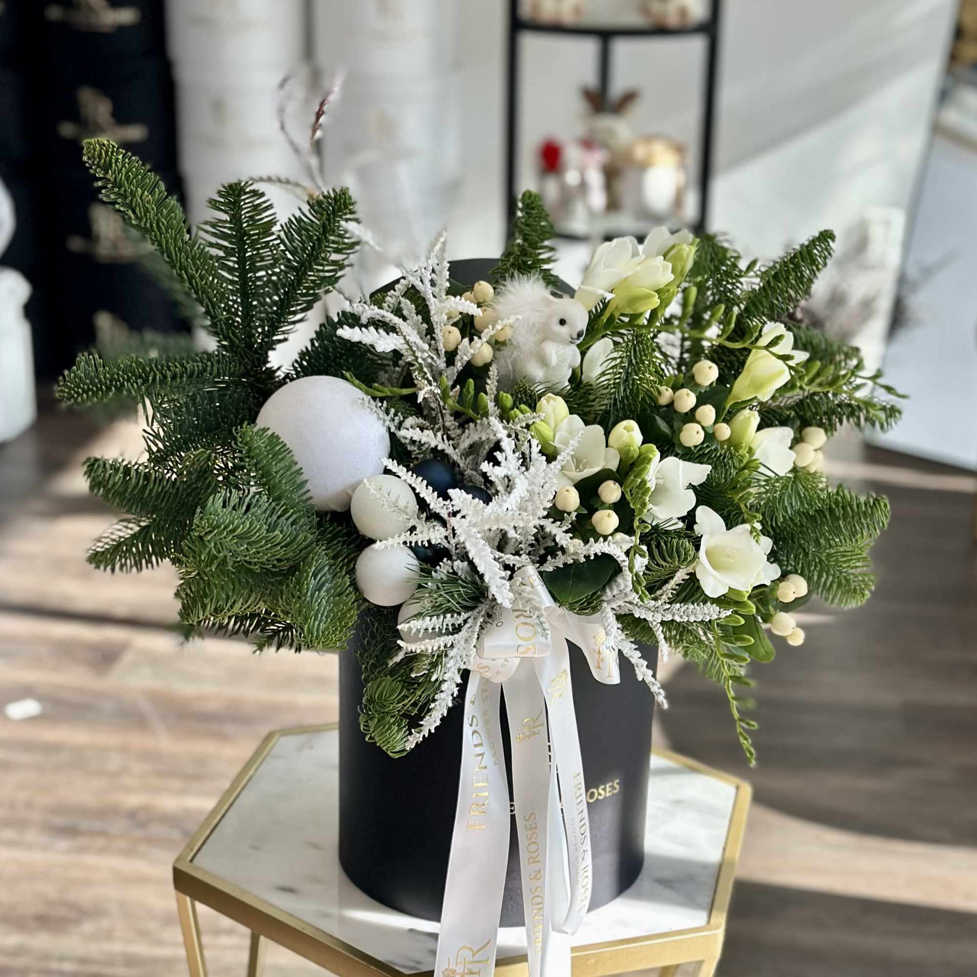 White flowers and evergreen branches arranged in a black hatbox with ribbon.