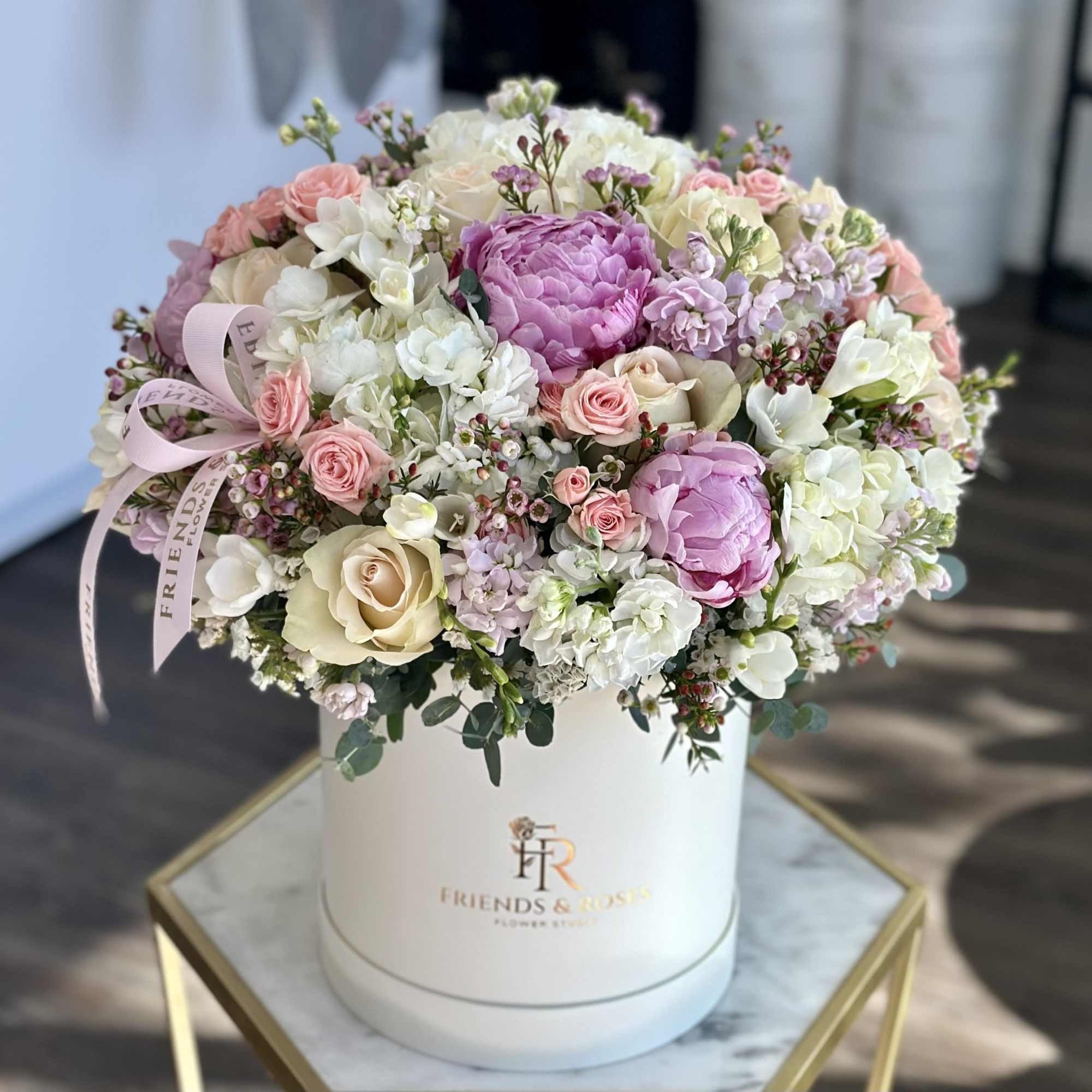 Round pastel flower arrangement in a white hat box with pink ribbon