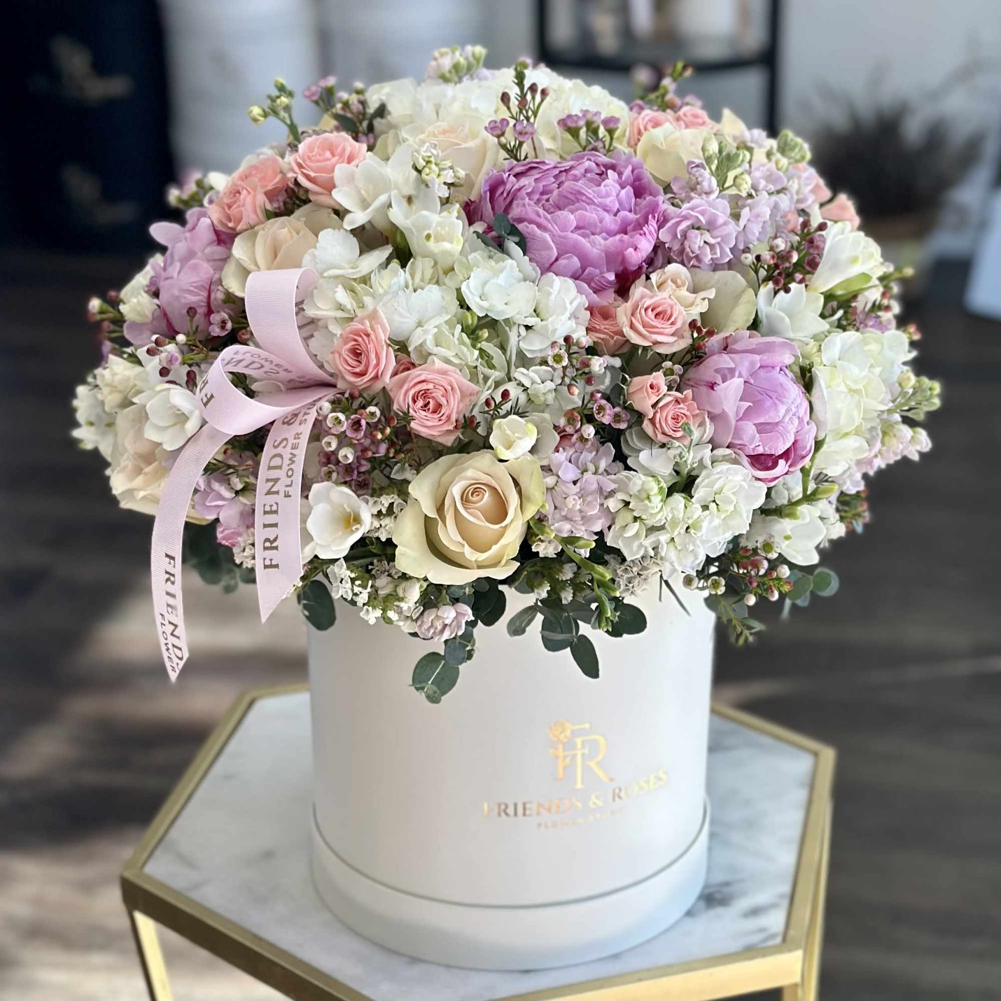 Round pastel flower arrangement in a white hat box with a pink ribbon