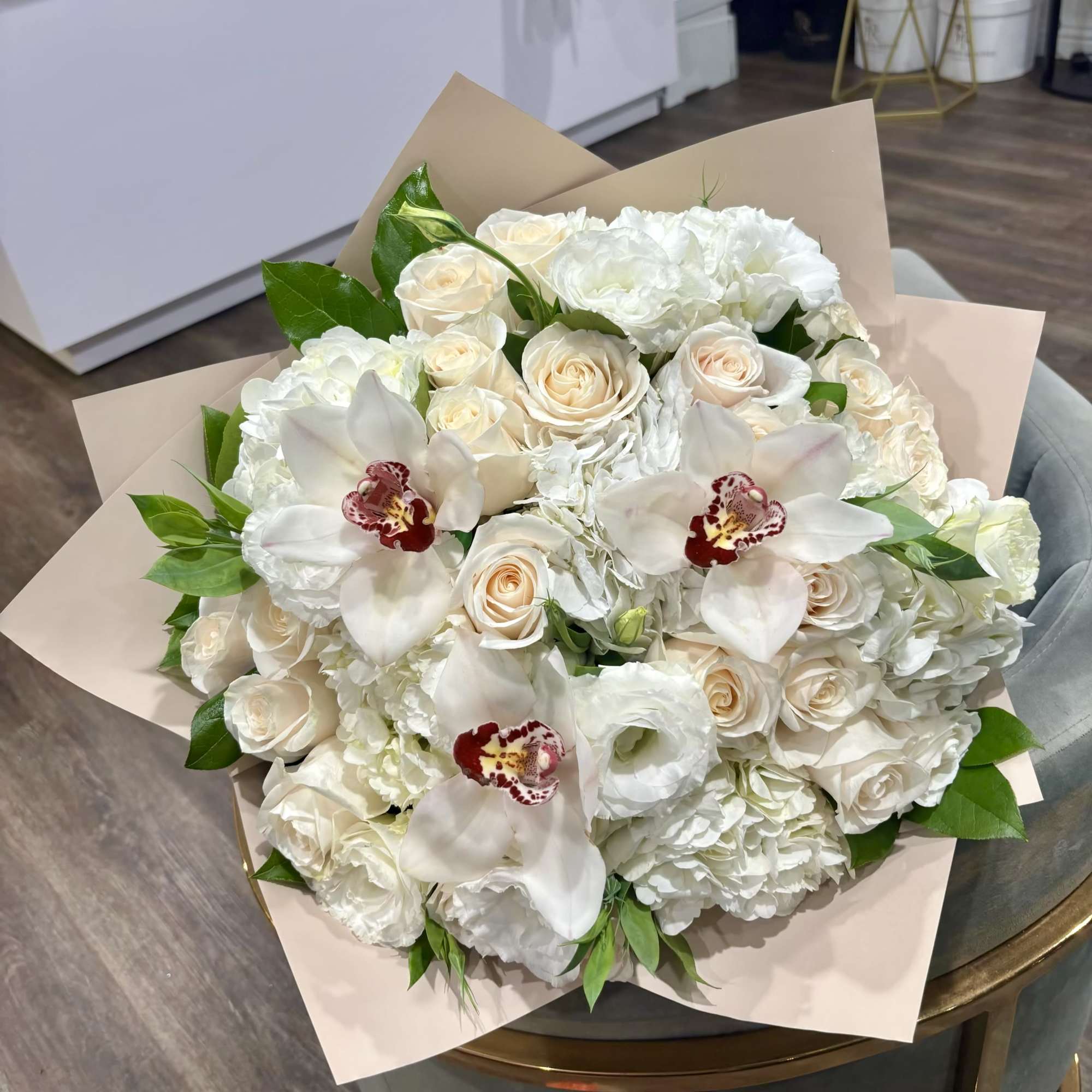 White bouquet of roses, hydrangeas, and orchids wrapped in beige paper