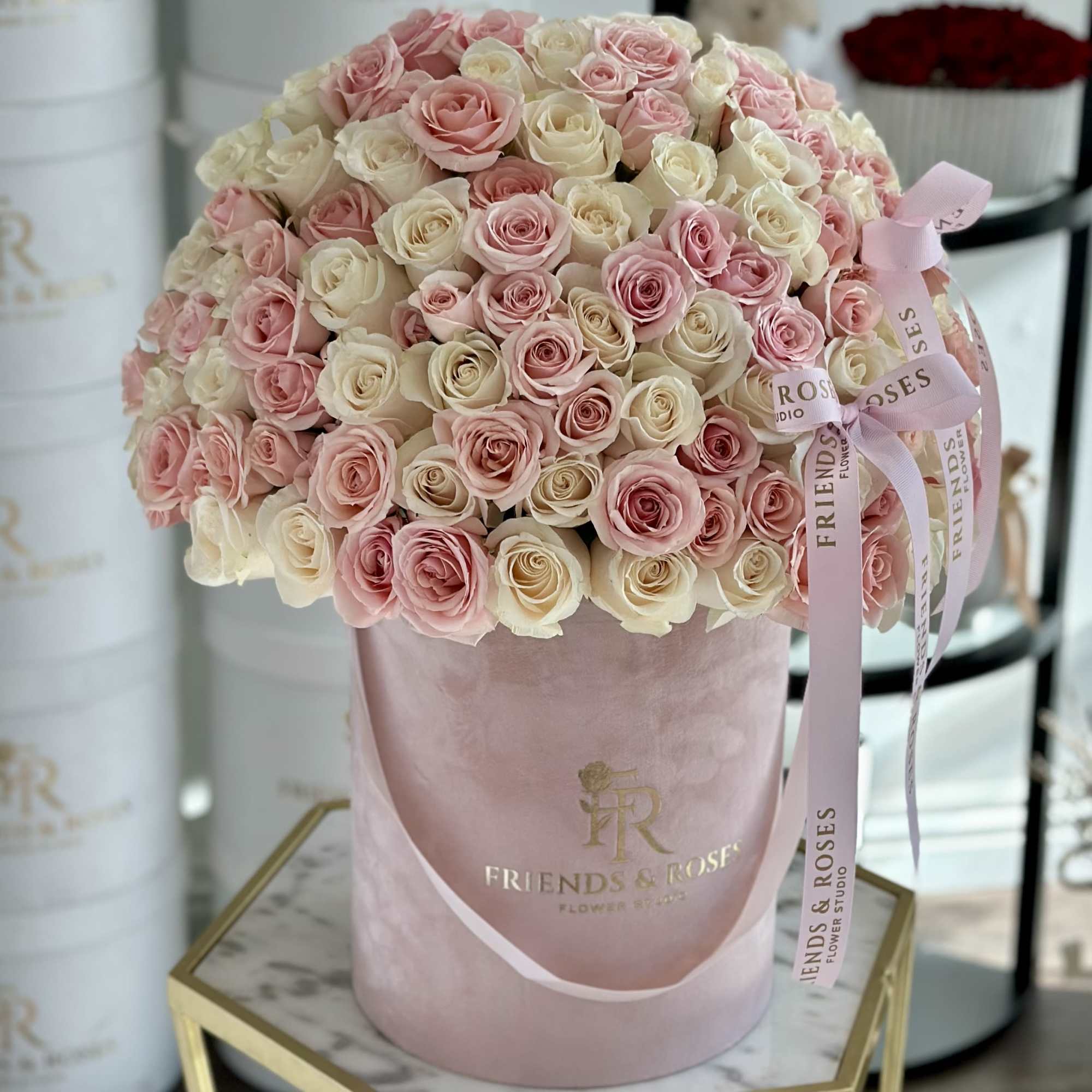 Pink and cream roses arranged in a round pink hat box with ribbon.