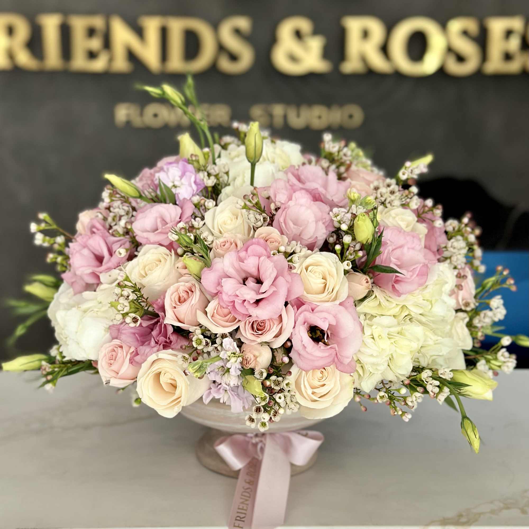 Pink and cream rose bouquet in a pedestal bowl with a ribbon