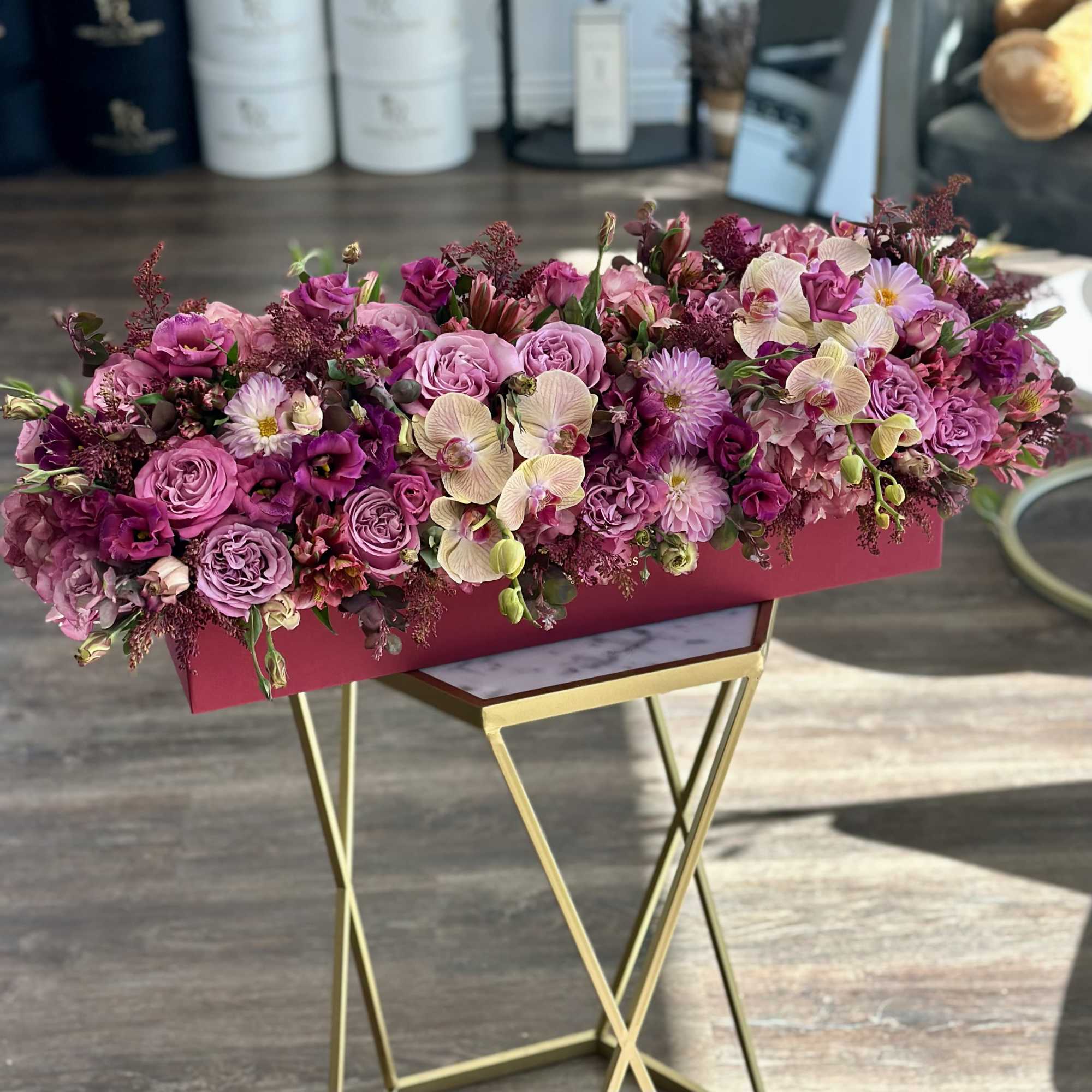 Pink and purple floral arrangement in a rectangular box on a gold stand
