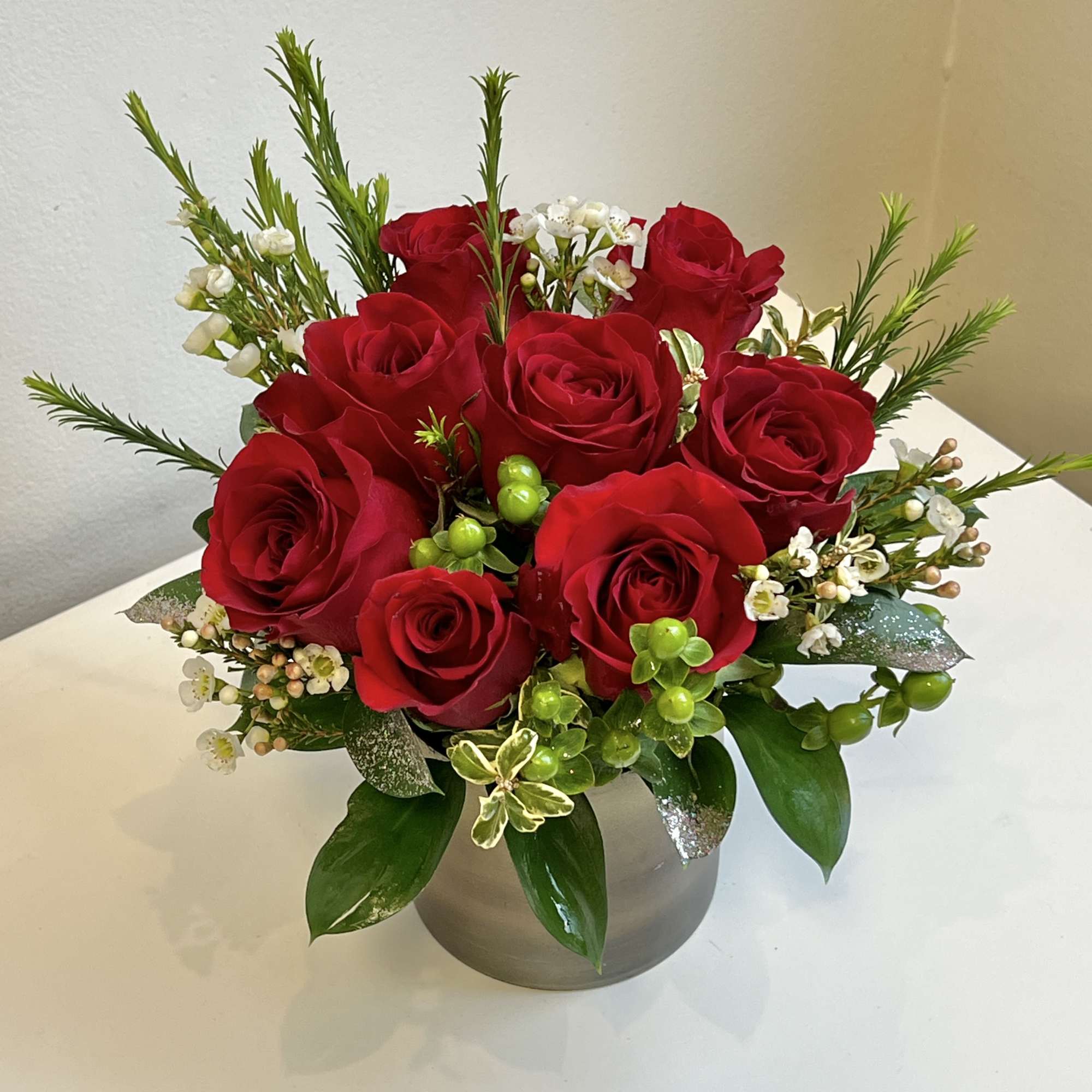 Red roses arranged in a round gray vase with white accent flowers