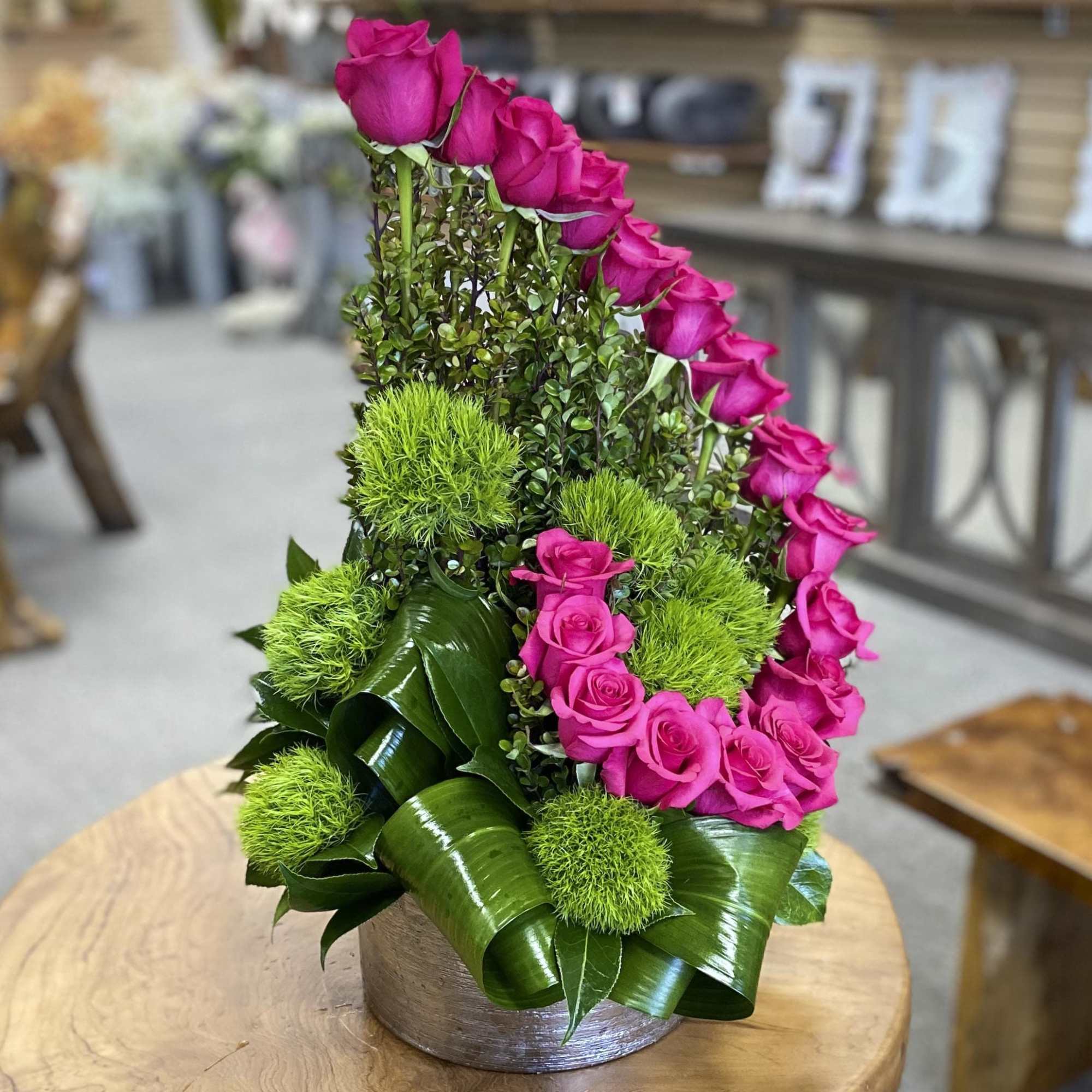 Pink roses arranged in a curved design with green pom-pom accents in a round vase