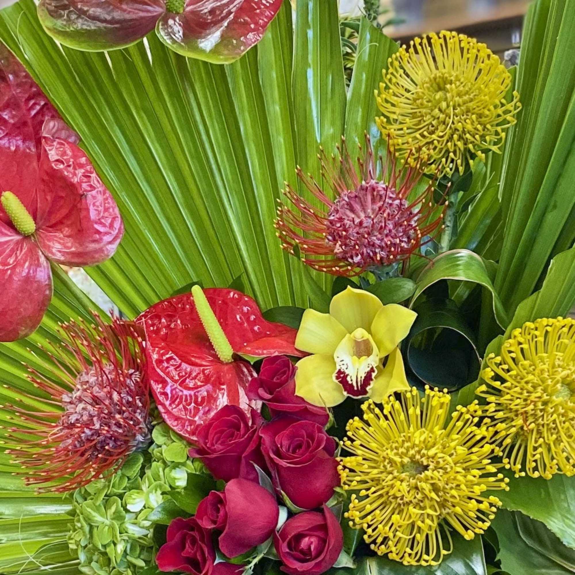 Tropical bouquet with red anthuriums, yellow pincushion blooms, and pink roses