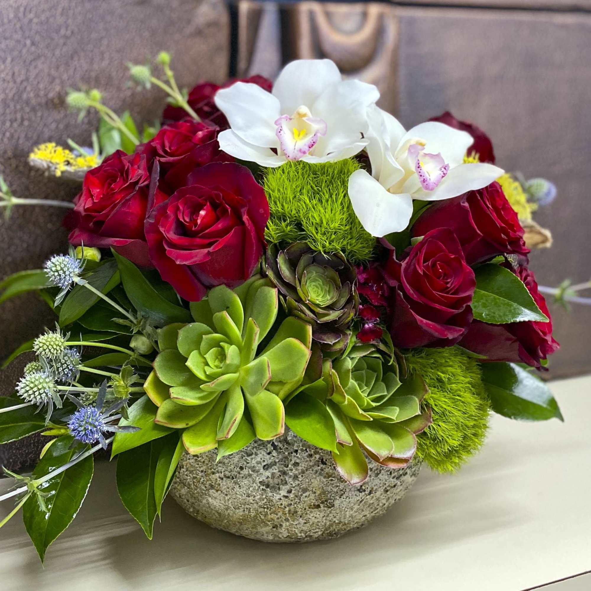 Red roses and white orchids arranged with succulents in a stone bowl