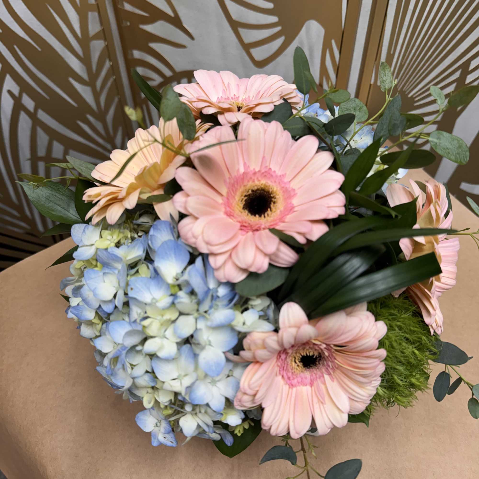 Bouquet of pink gerbera daisies and blue hydrangeas wrapped in brown paper