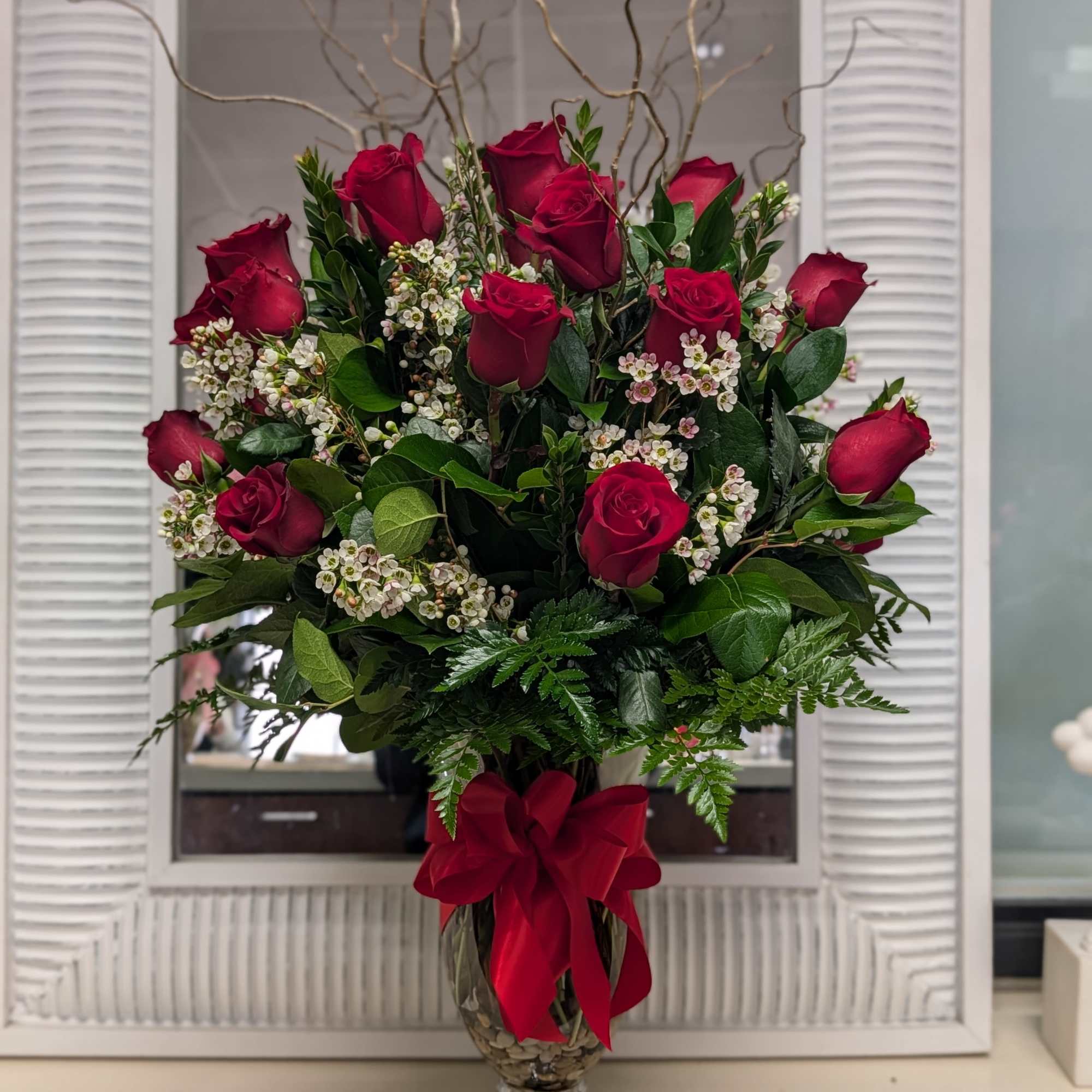 Red rose arrangement in a glass vase with a red ribbon
