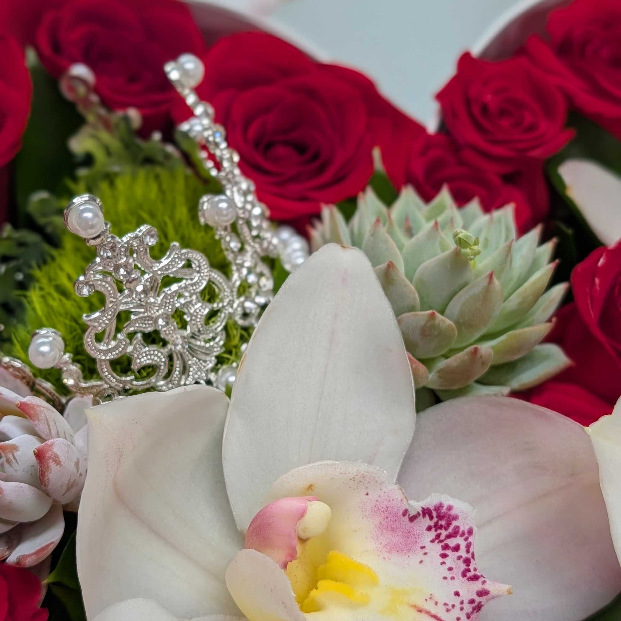 Arrangement of red roses, white orchid, succulents, and a silver tiara accent