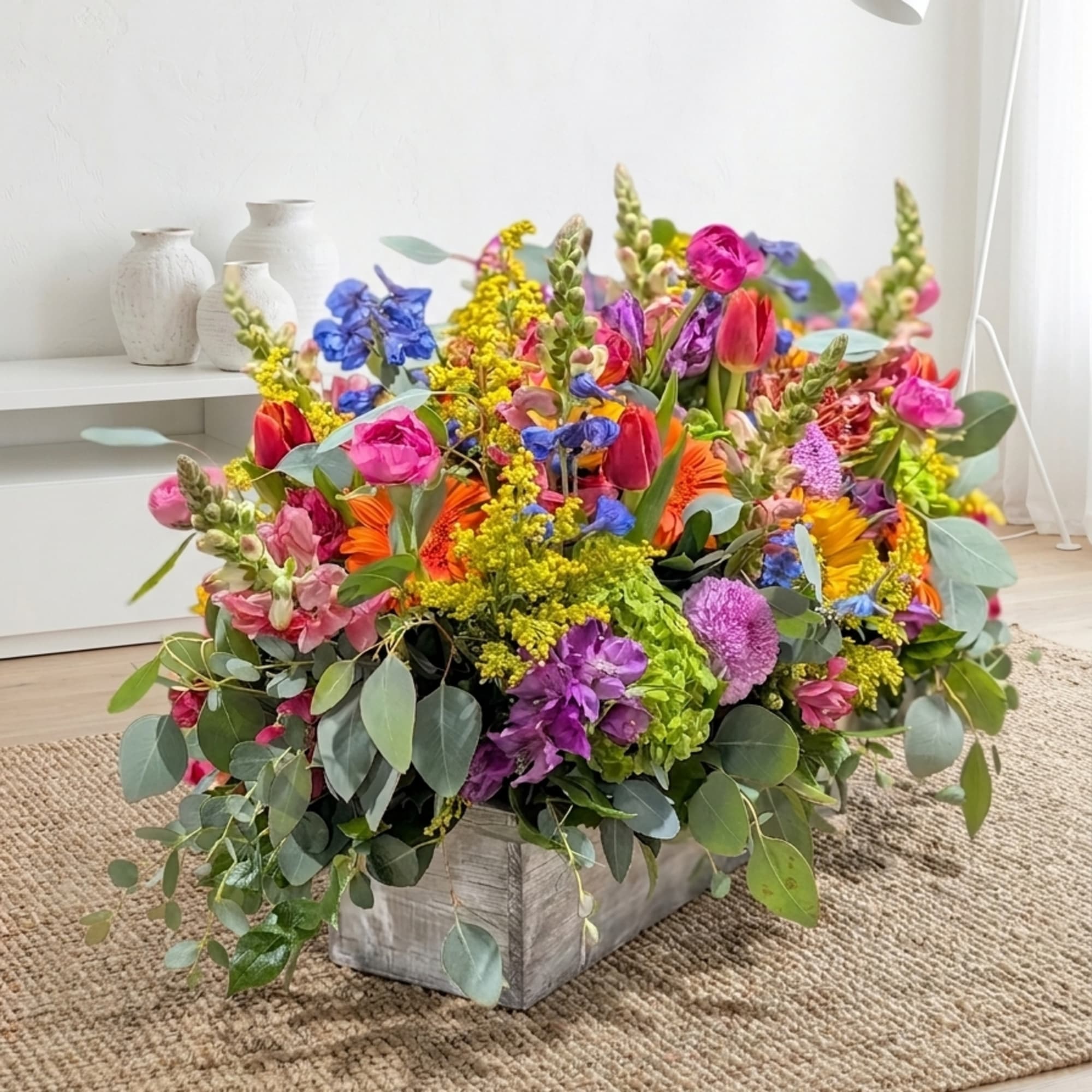 Low rectangular centerpiece of bright mixed flowers in a rustic wooden box