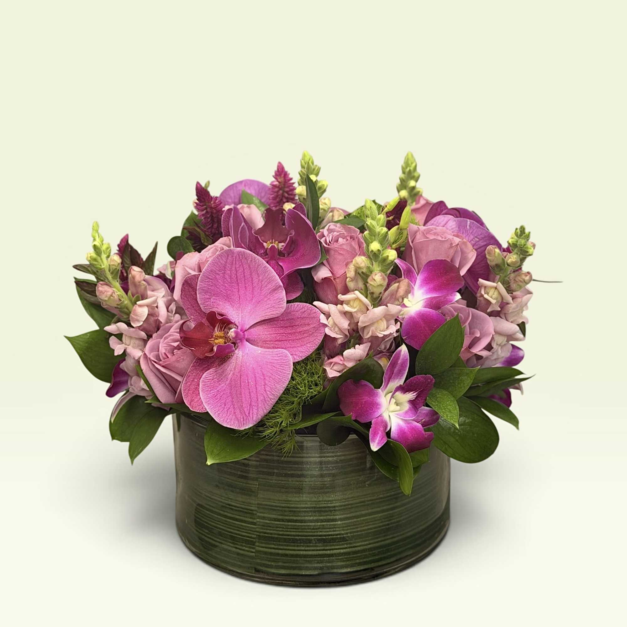 Pink orchids and roses arranged in a low dark vase