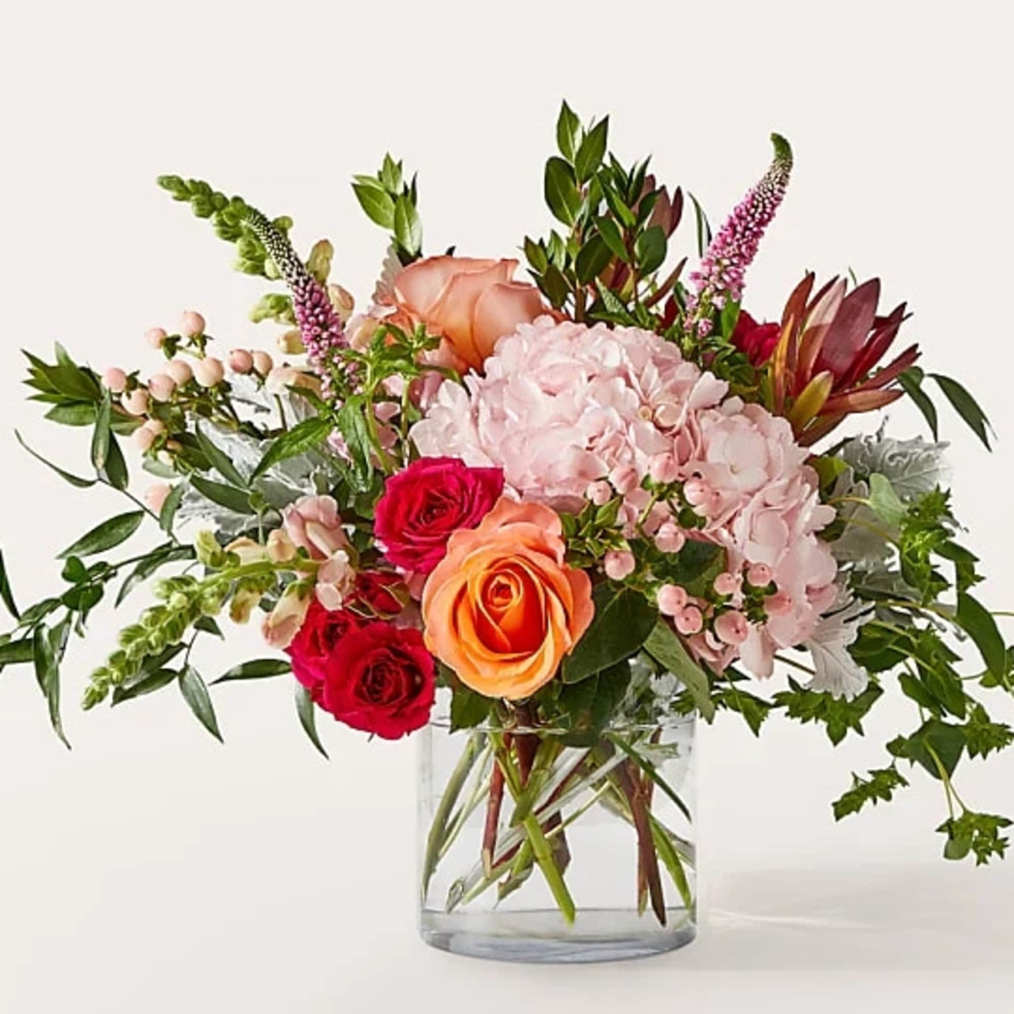 Mixed bouquet of pink, peach, and red flowers in a clear glass vase