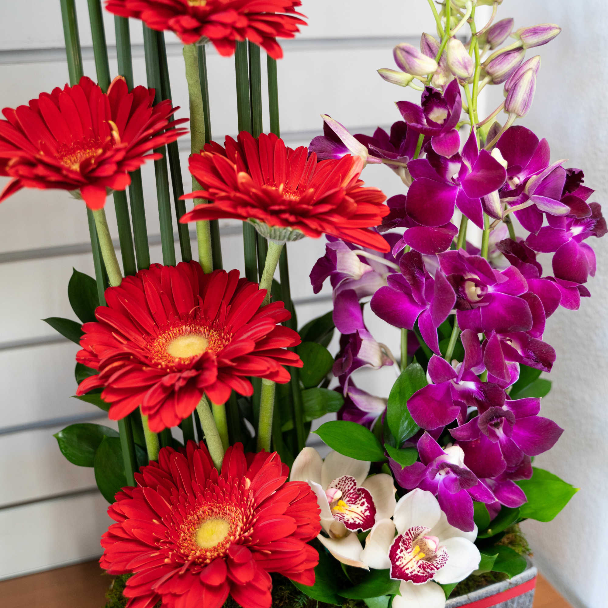 Red gerbera daisies and purple orchids in a rectangular container