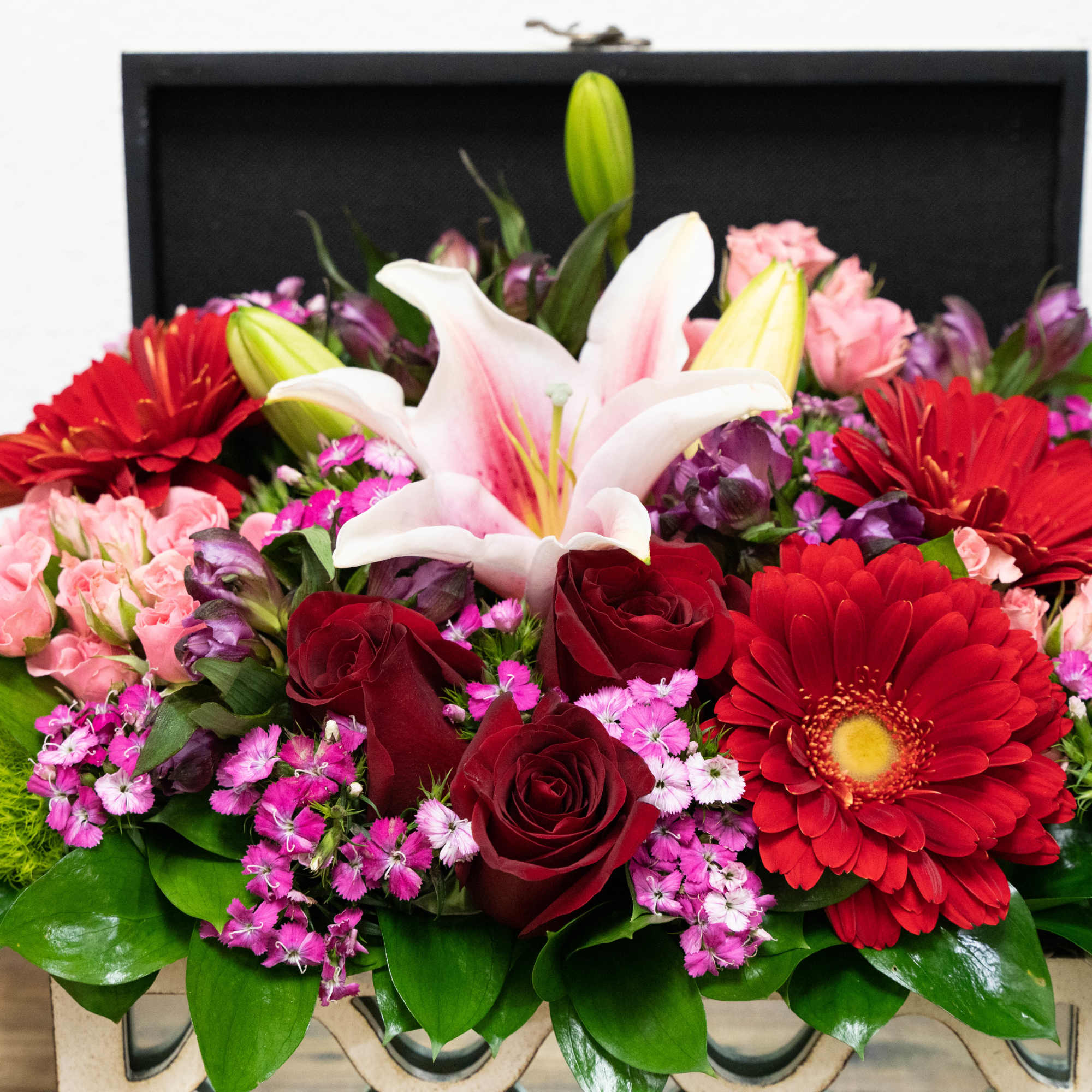 Mixed bouquet with red gerbera daisies, roses, and a white lily in a black box