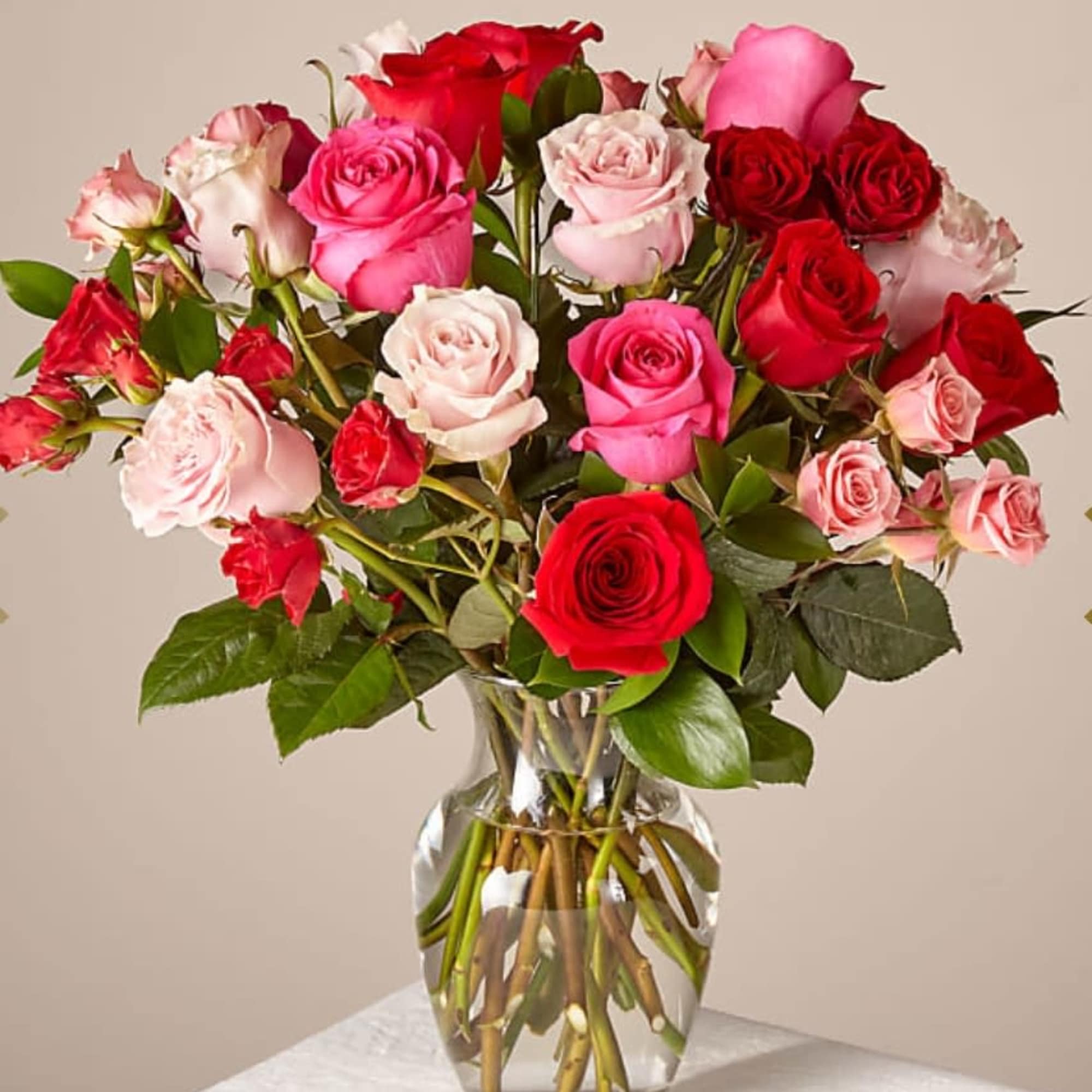 Arrangement of red and pink roses in a clear glass vase on a white surface