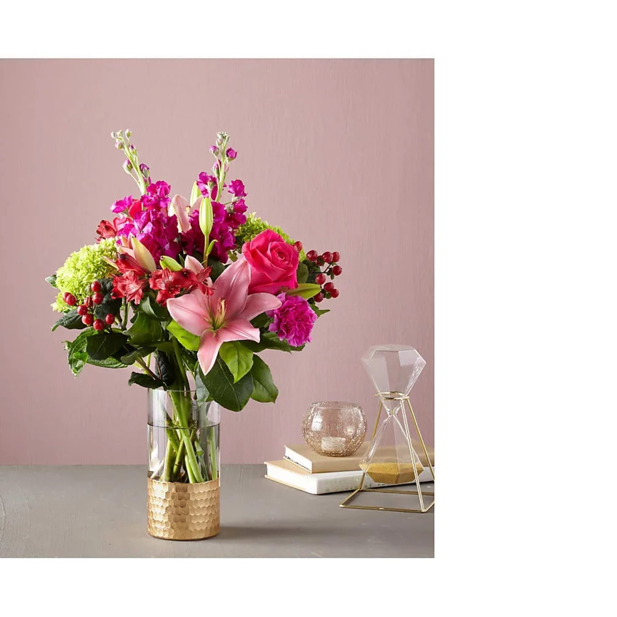 Tall mixed bouquet of pink lilies, roses, carnations, and green hydrangea in a glass vase with gold base