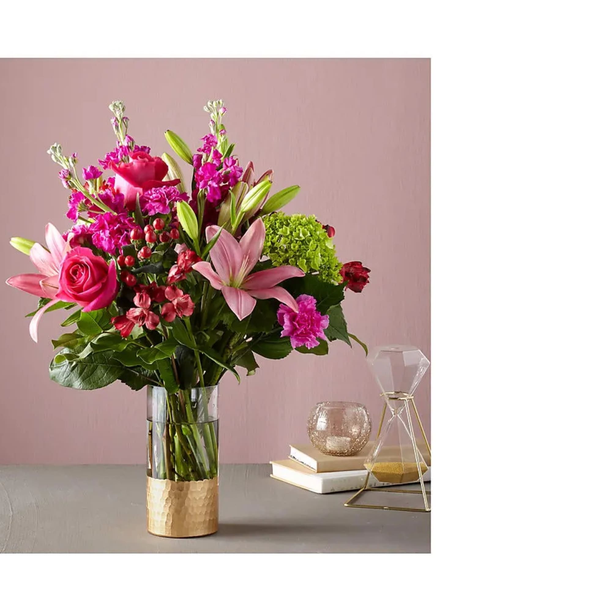 Tall arrangement of pink lilies, roses, and mixed blooms in a clear glass vase with gold base
