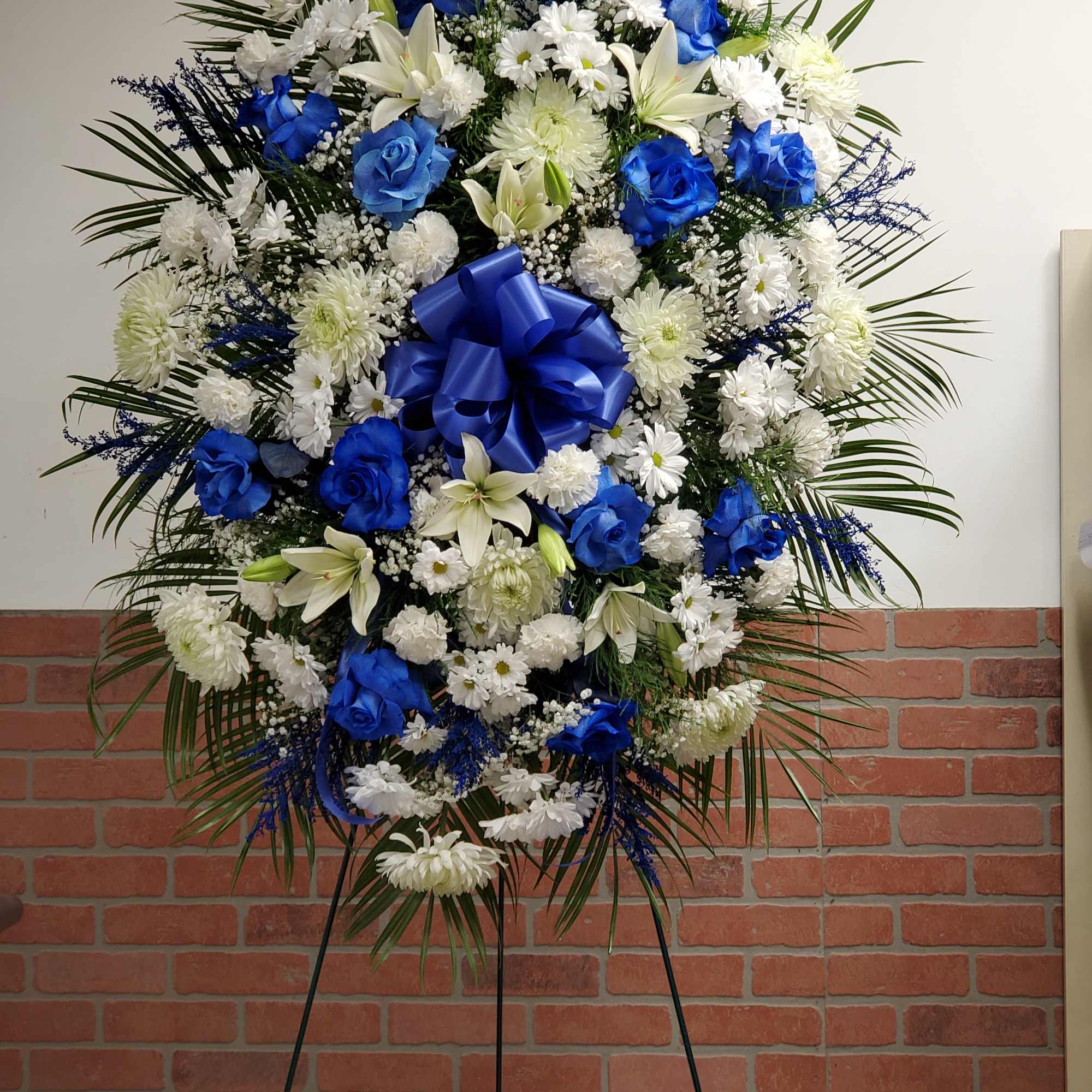 Large blue and white standing spray with roses, lilies, and mums on an easel.