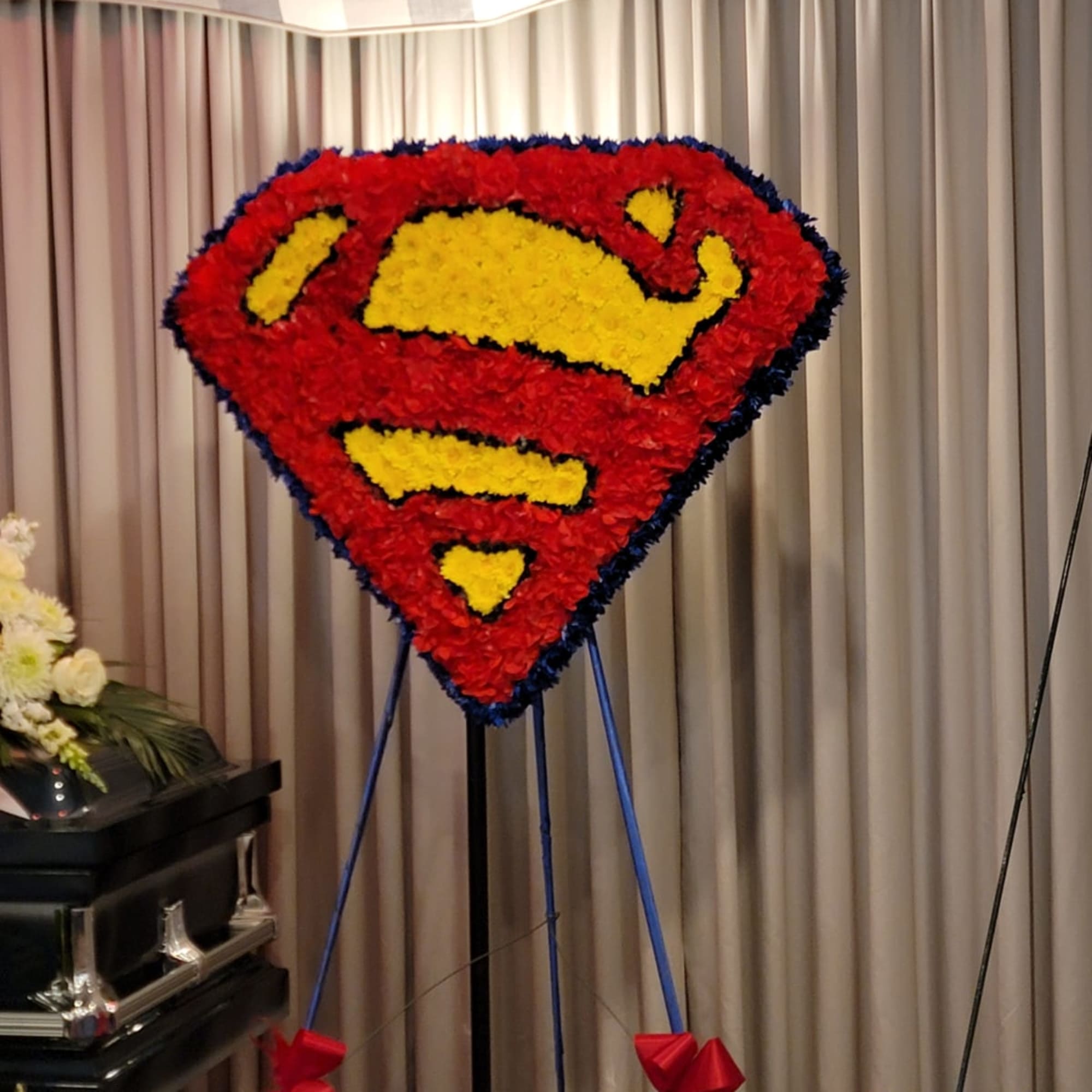 Standing funeral spray of red and yellow flowers in a hero emblem shape on a blue easel.