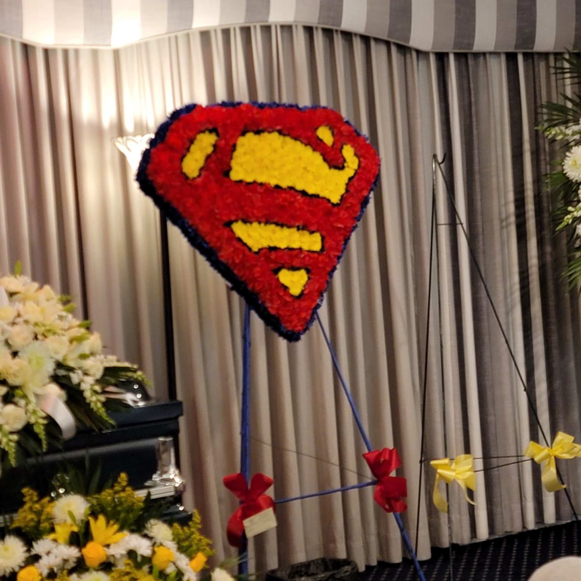 Superhero emblem–shaped red and yellow standing spray on an easel at a funeral service