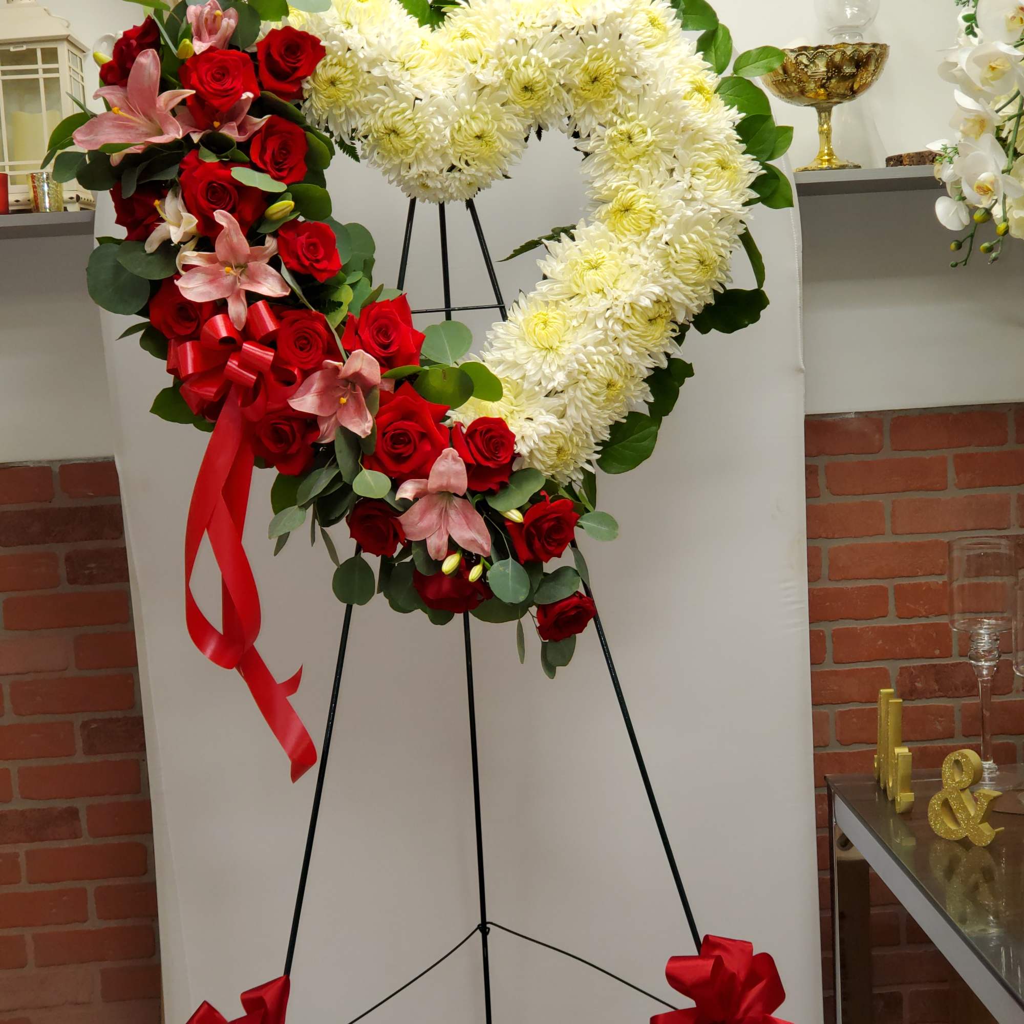 Heart-shaped standing wreath of white mums with red roses and pink lilies on a metal easel