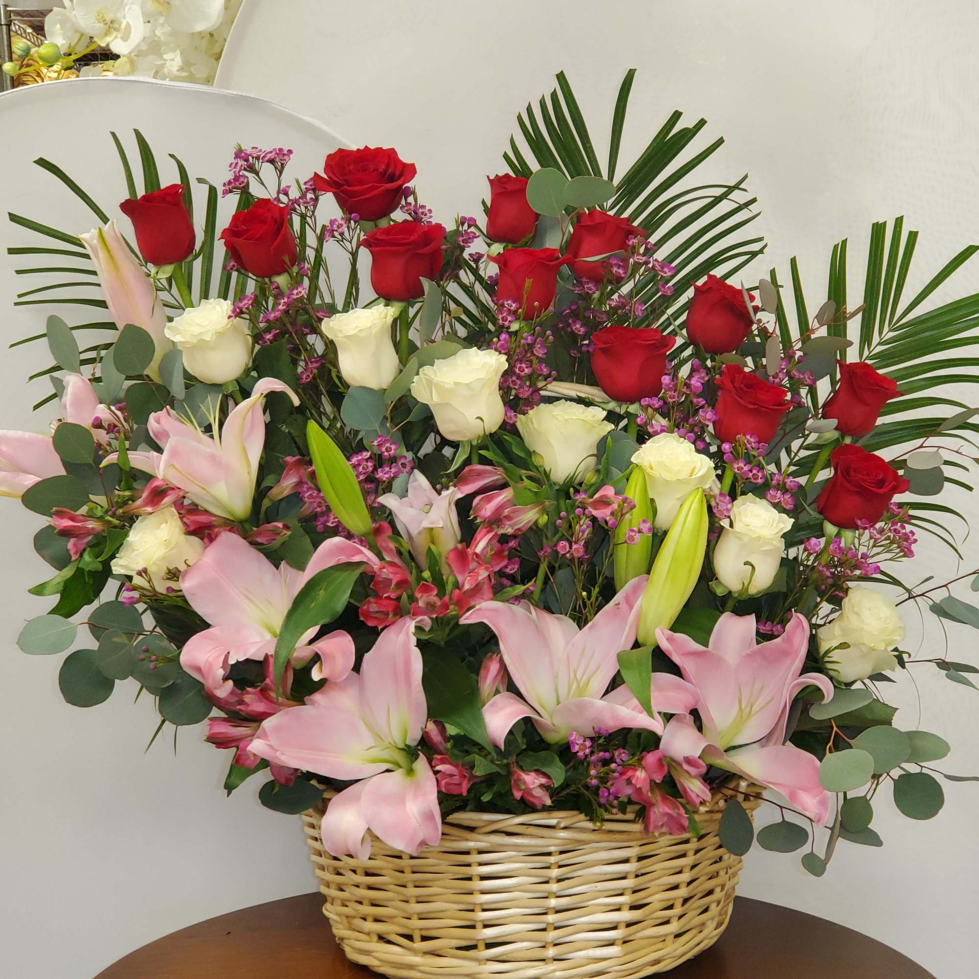 Large basket arrangement of red and white roses with pink lilies and mixed filler flowers.
