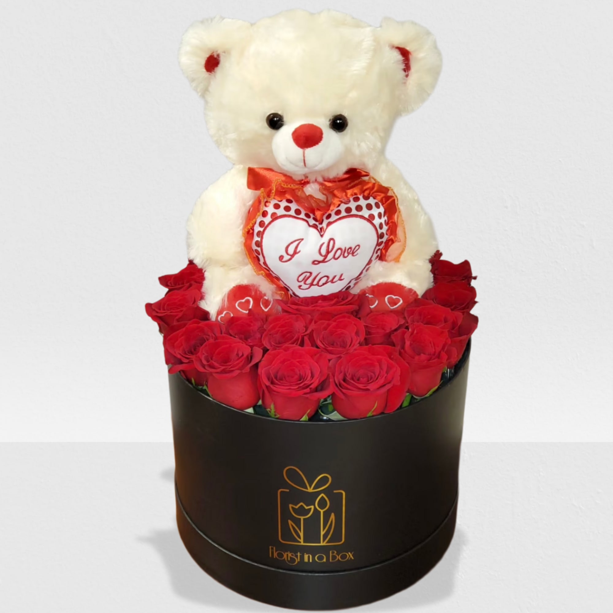 Black hat box of red roses topped with a white teddy bear holding an 'I Love You' heart pillow