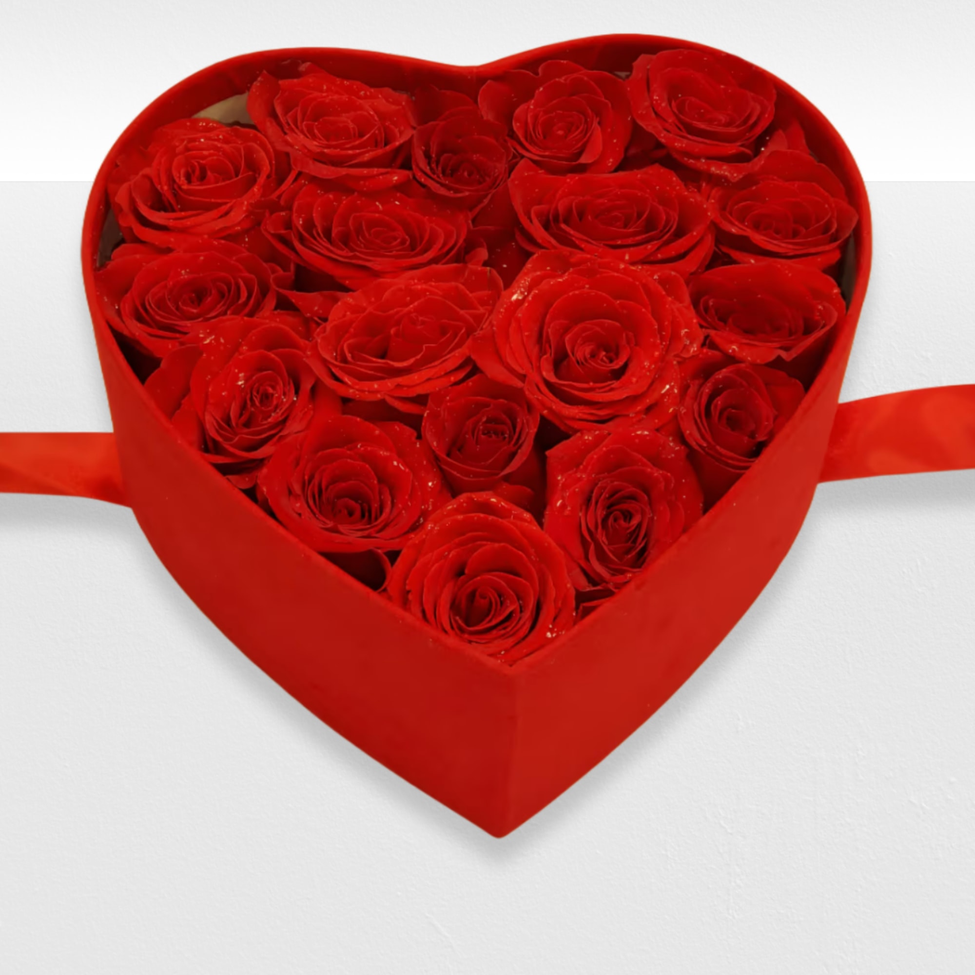 Red roses arranged inside a red heart-shaped box with side ribbons