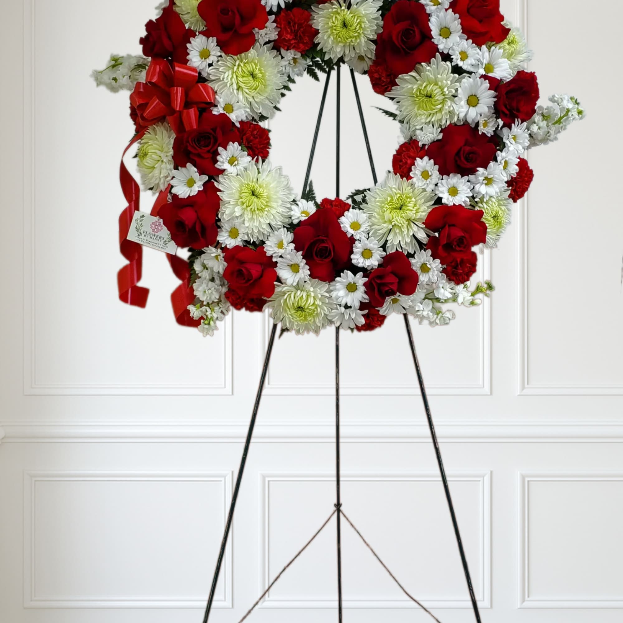 Large round standing wreath of red roses and white daisies with red bows on a metal easel