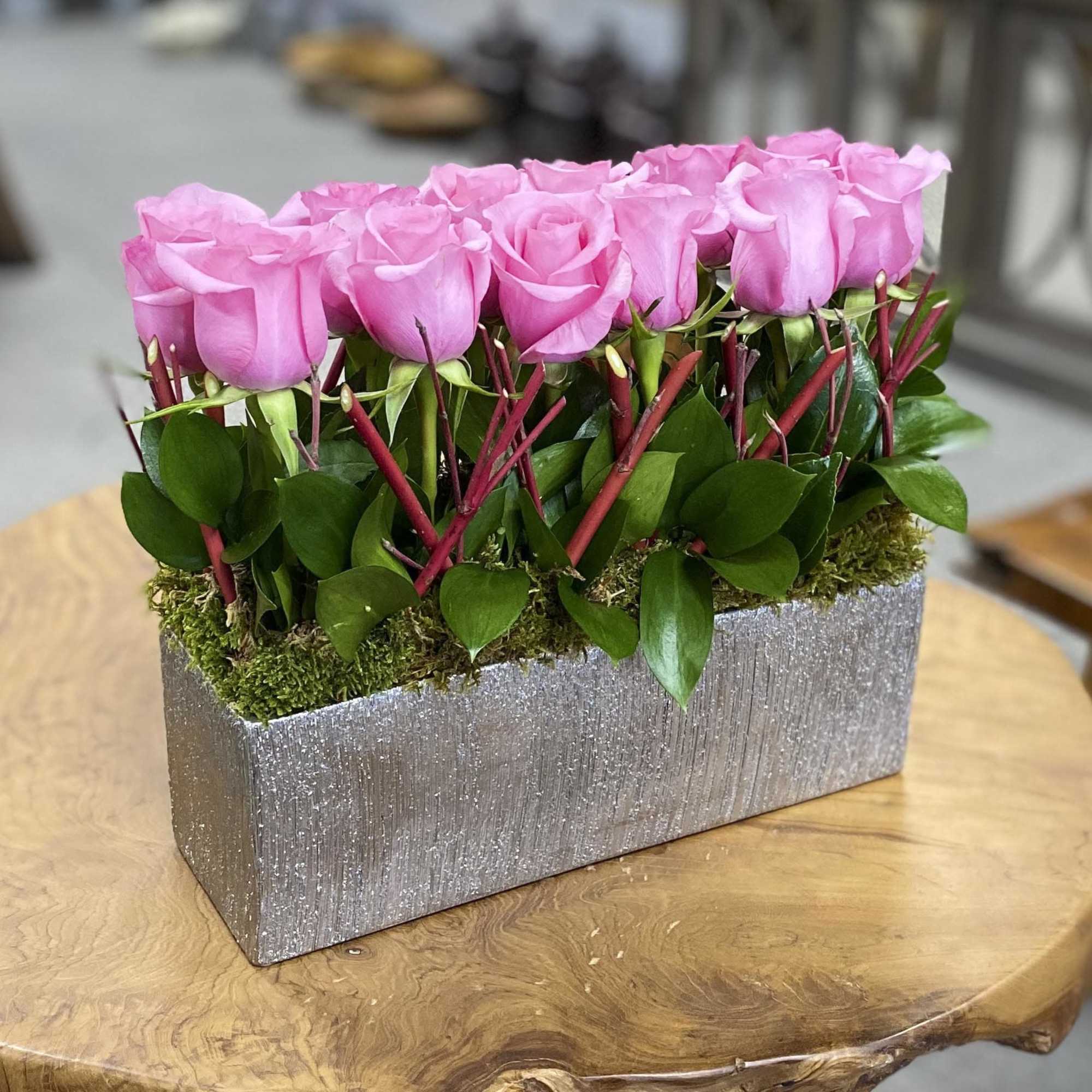 Pink roses arranged in a rectangular silver vase with moss