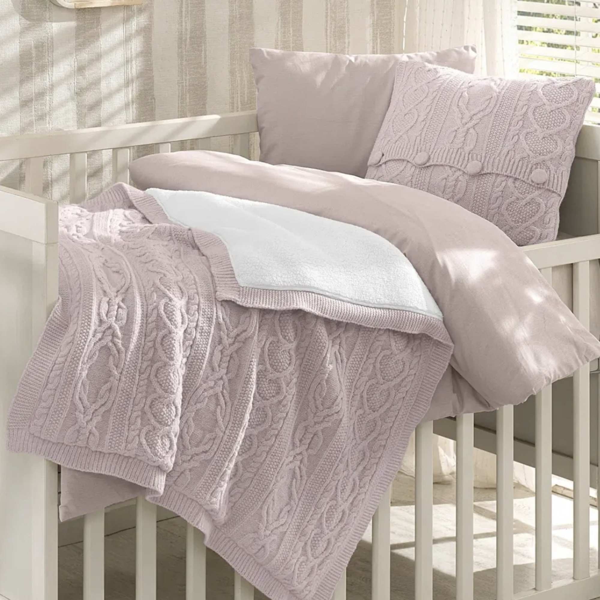 Pastel knit blanket and pillows arranged on a white crib