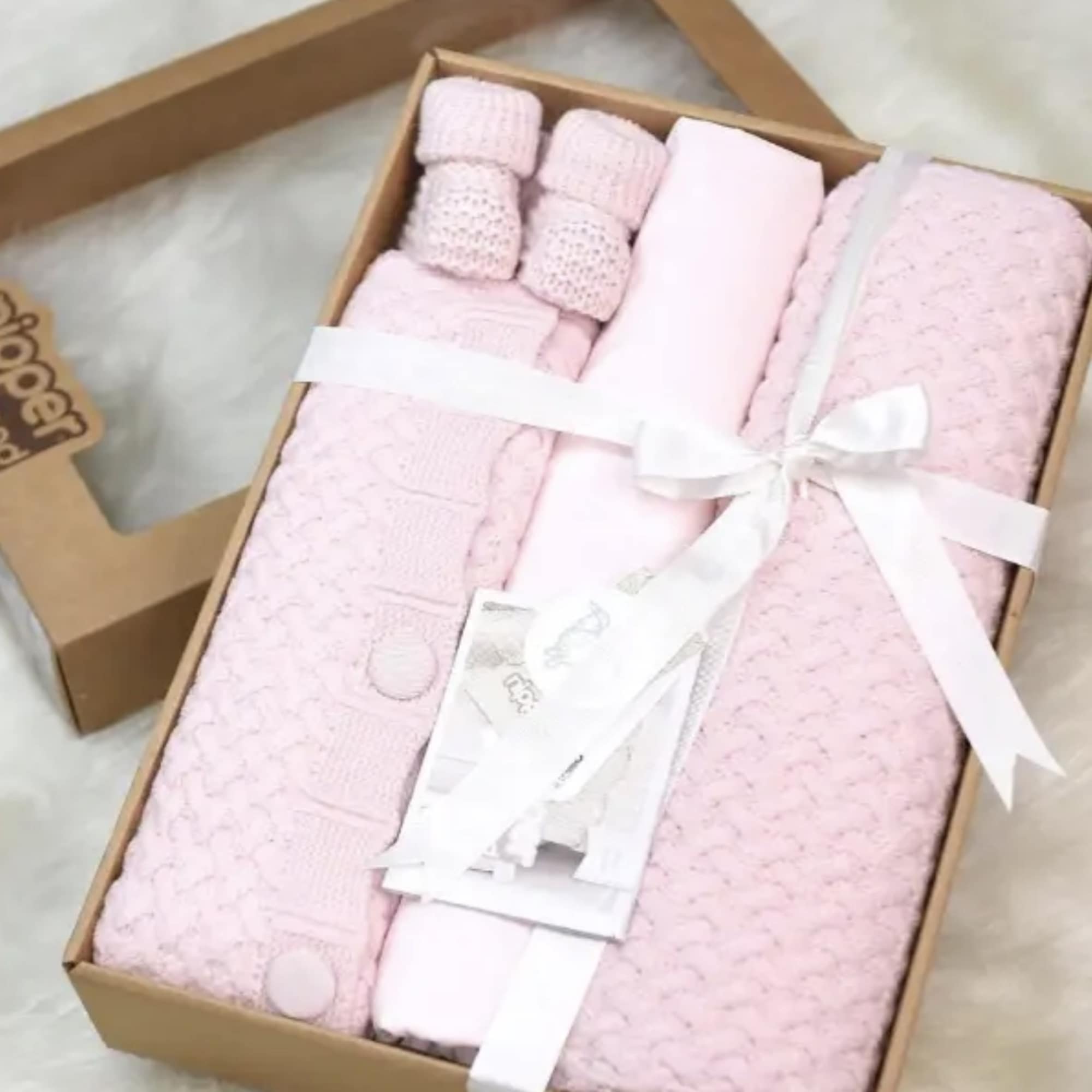 Gift box with folded pink baby clothes and accessories tied with a white ribbon