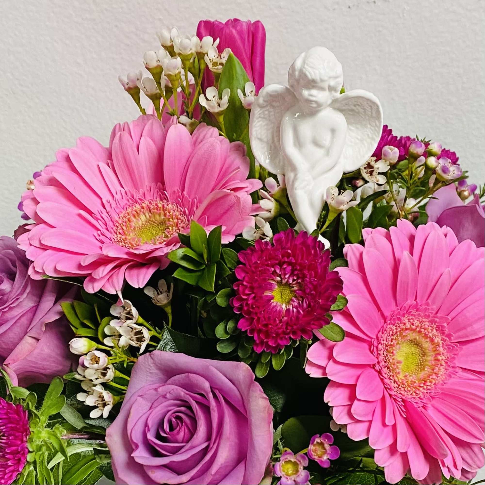 Pink gerbera daisies and purple roses with a small white angel figurine