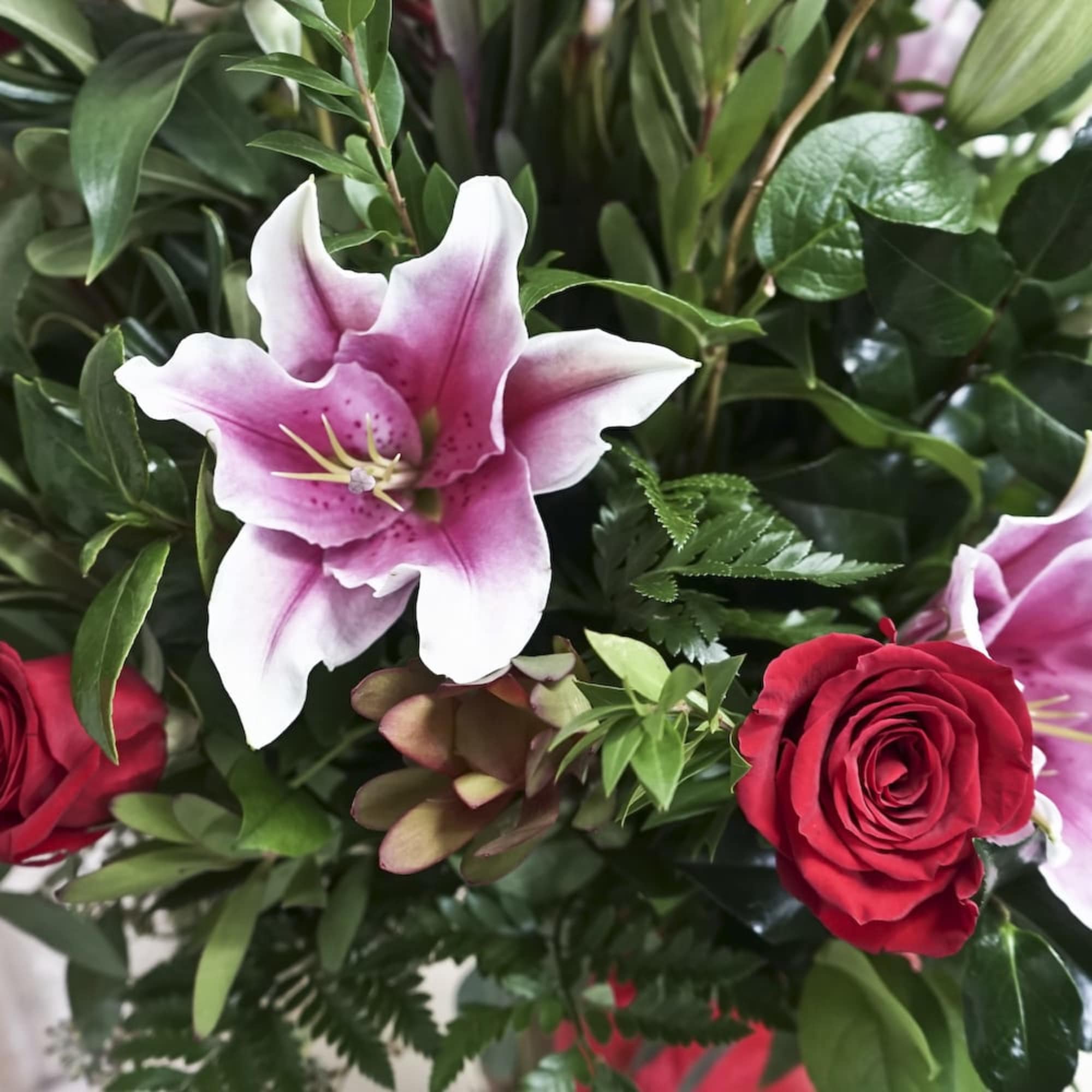 Bouquet with pink lilies and red roses among dense greenery