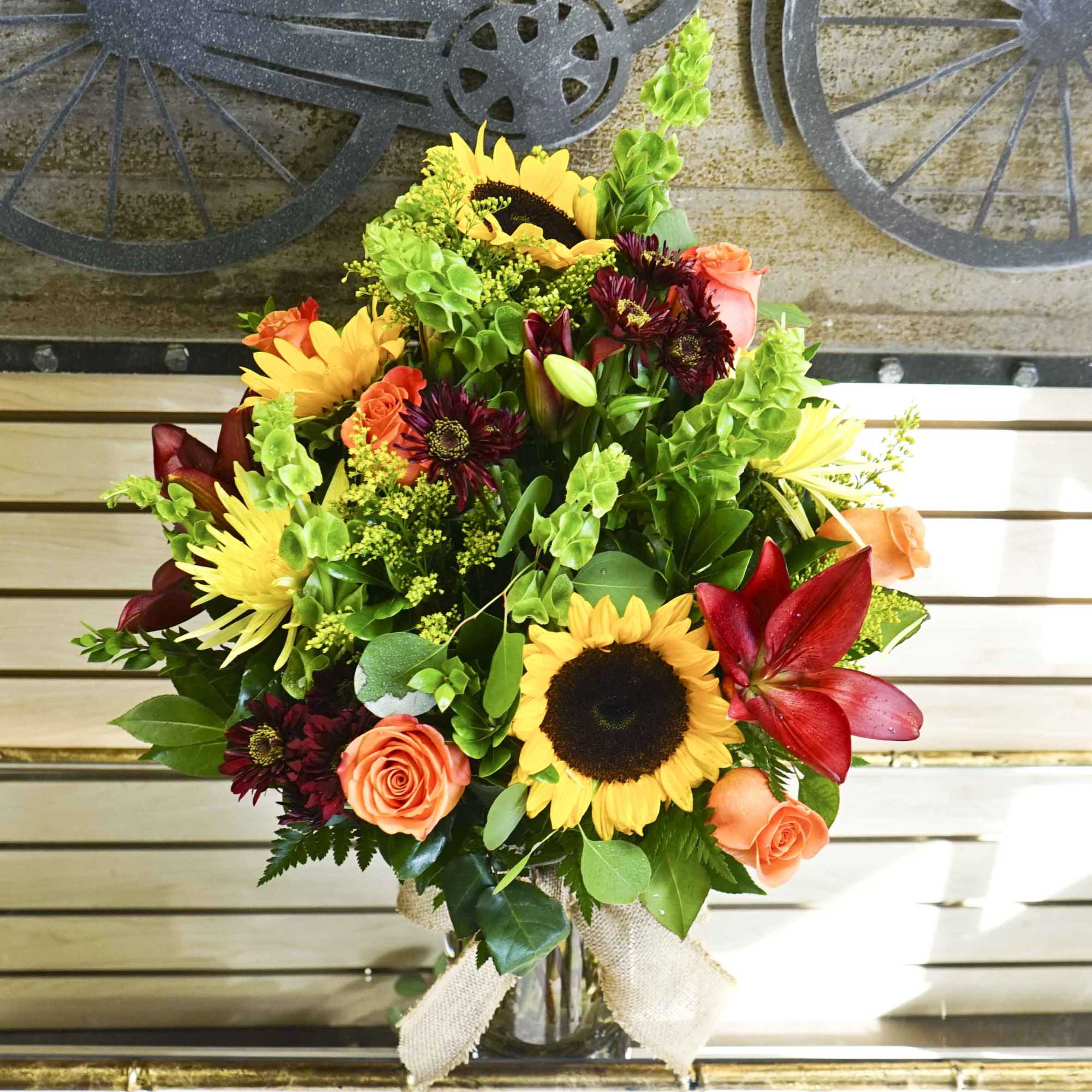 Bouquet of sunflowers, orange roses, and burgundy blooms in a glass vase
