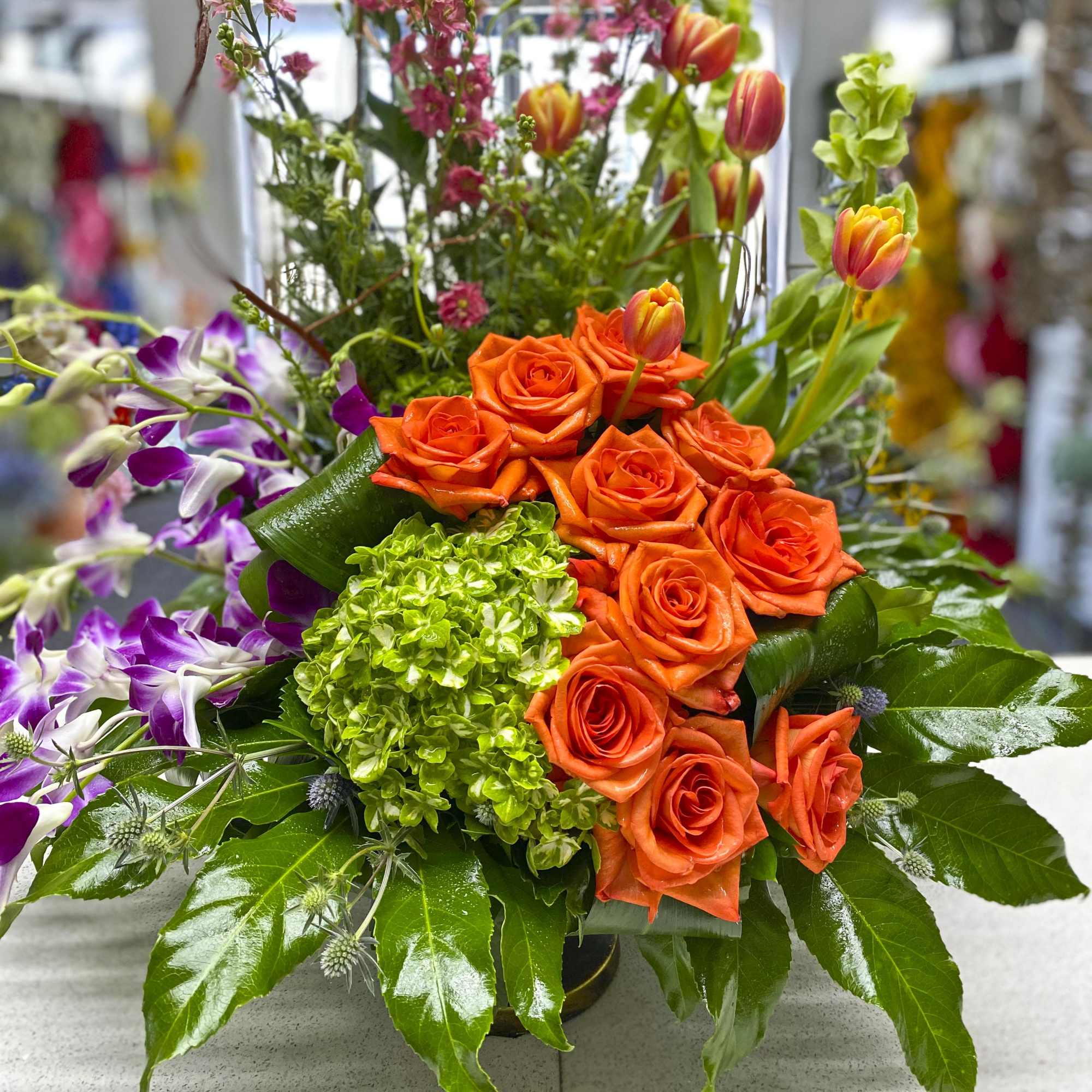 Orange roses and tulips arranged with purple orchids and green hydrangea.