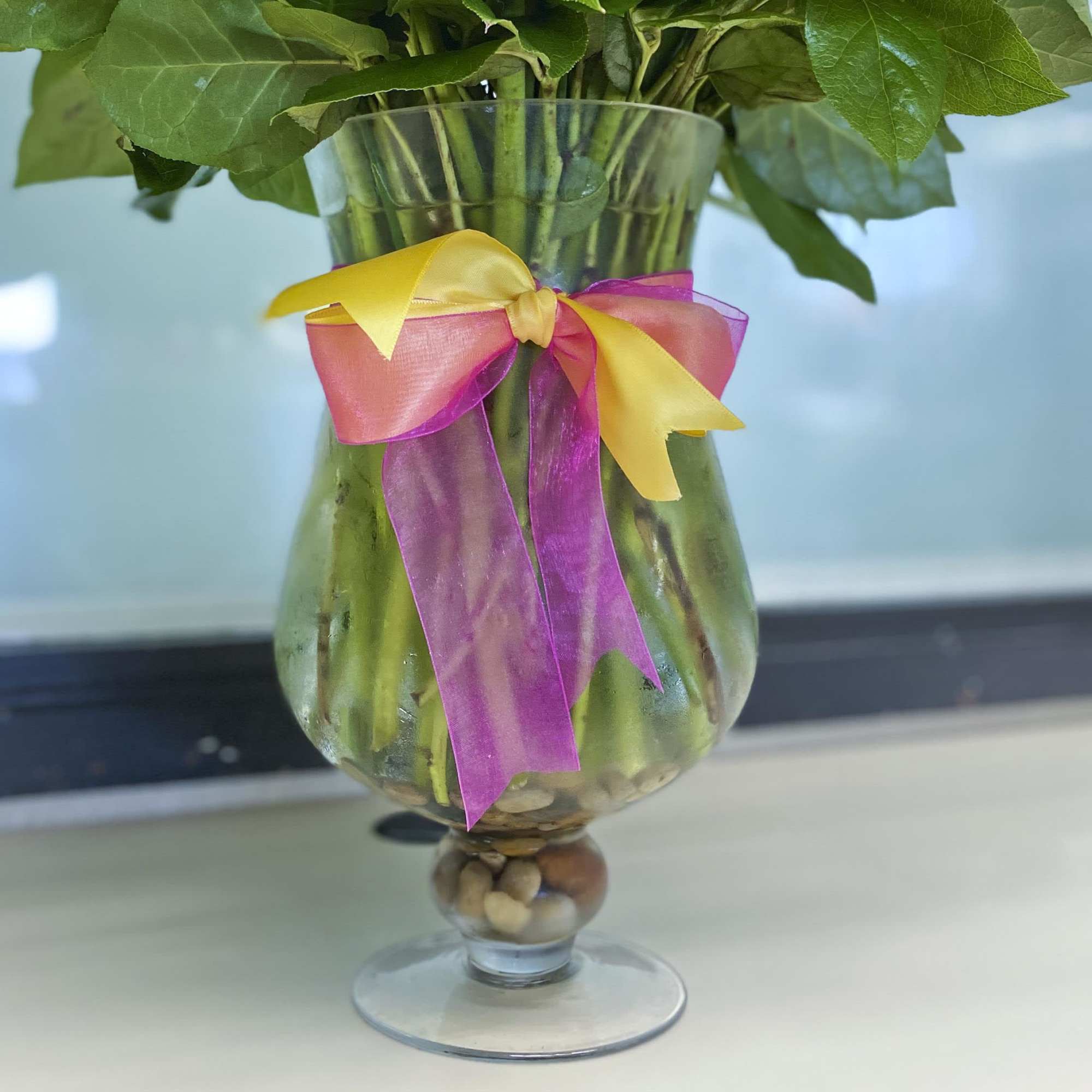 Bouquet of green-stemmed flowers in a glass vase with a pink and yellow ribbon