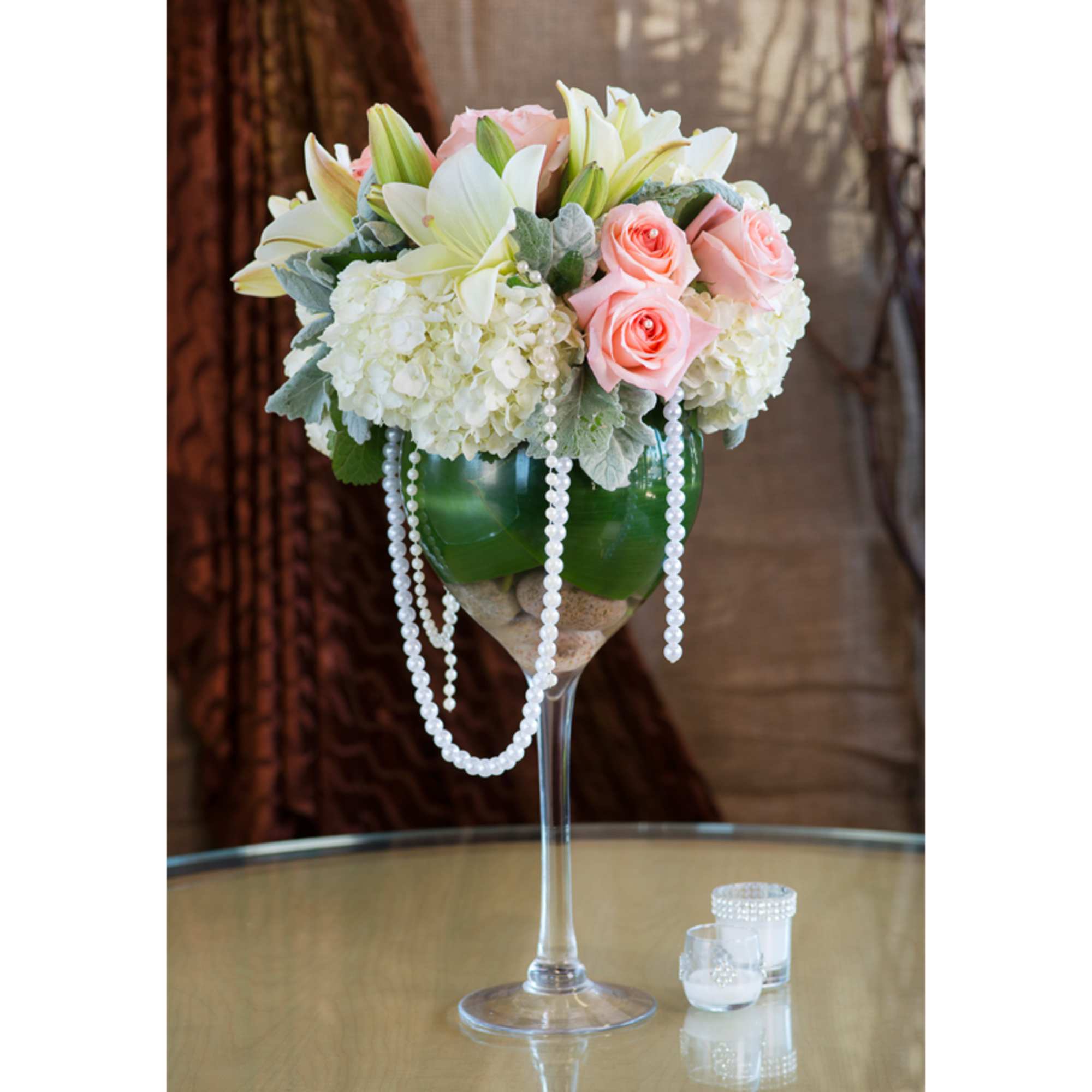Pink roses and white lilies in a tall glass vase with pearl strands