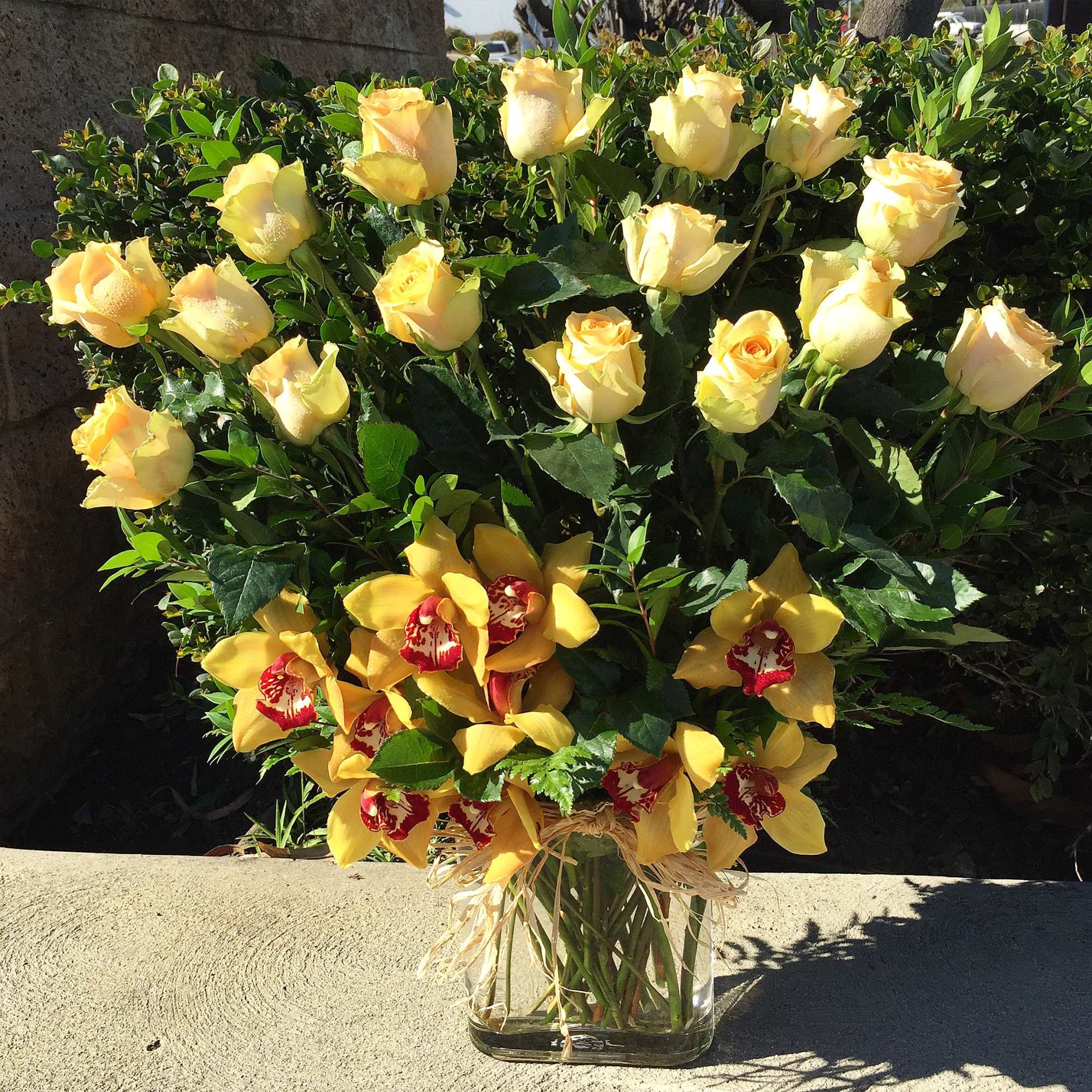 Yellow roses and orchids arranged in a clear glass vase