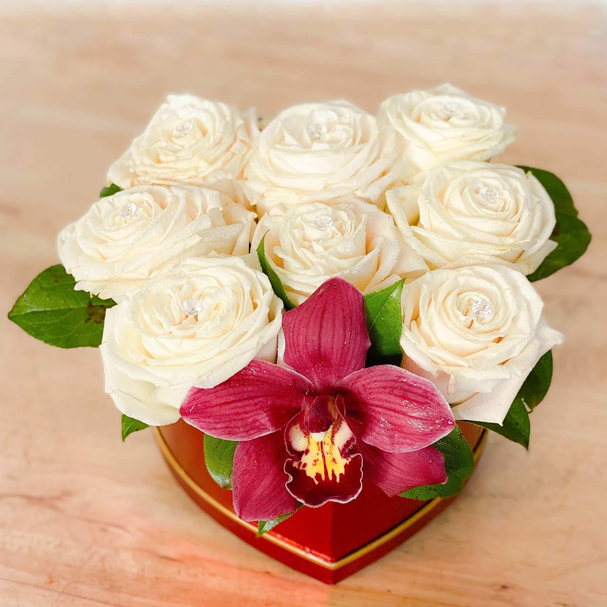 White roses with a deep pink orchid in a red heart-shaped box