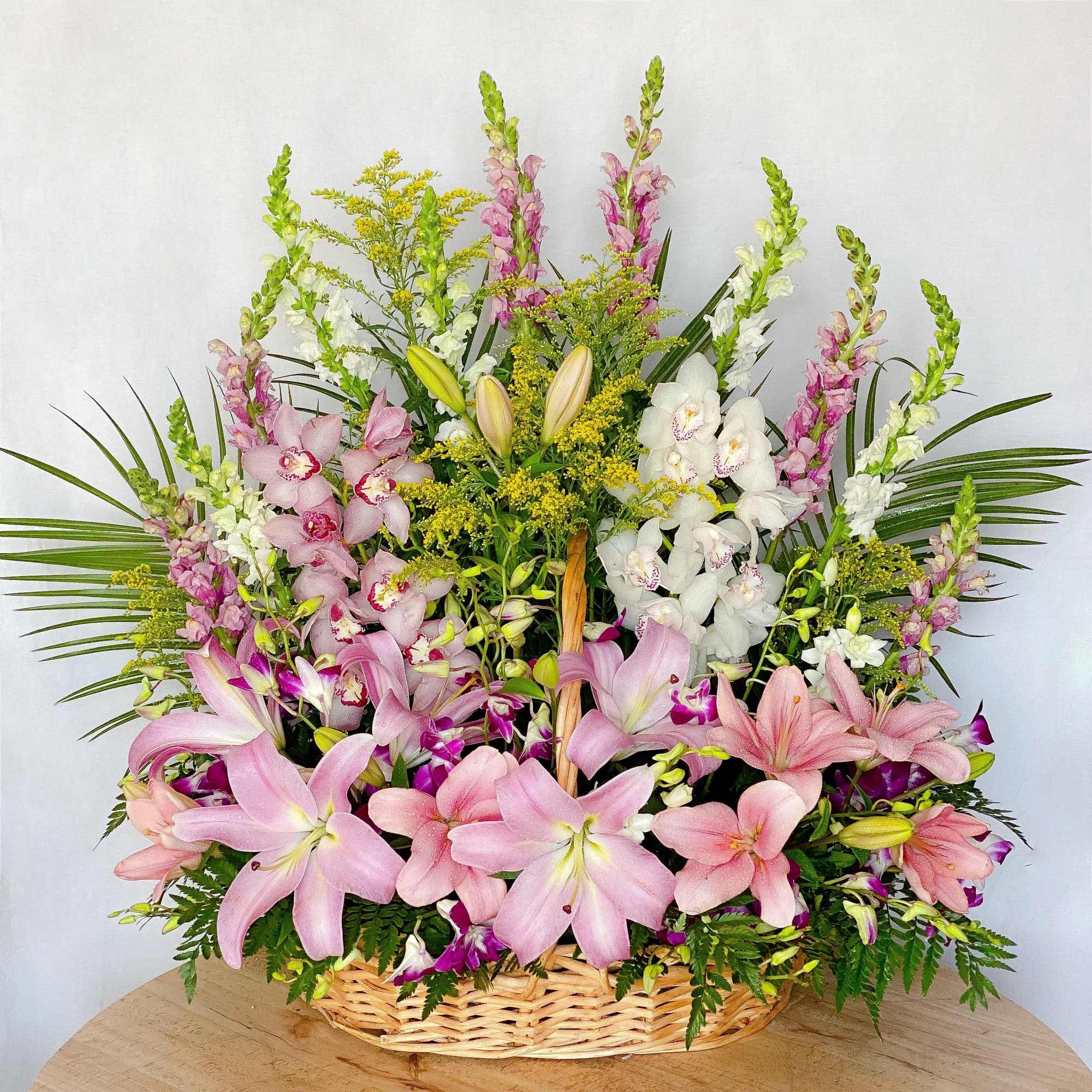 Large basket arrangement of pink lilies and white orchids with tall snapdragons