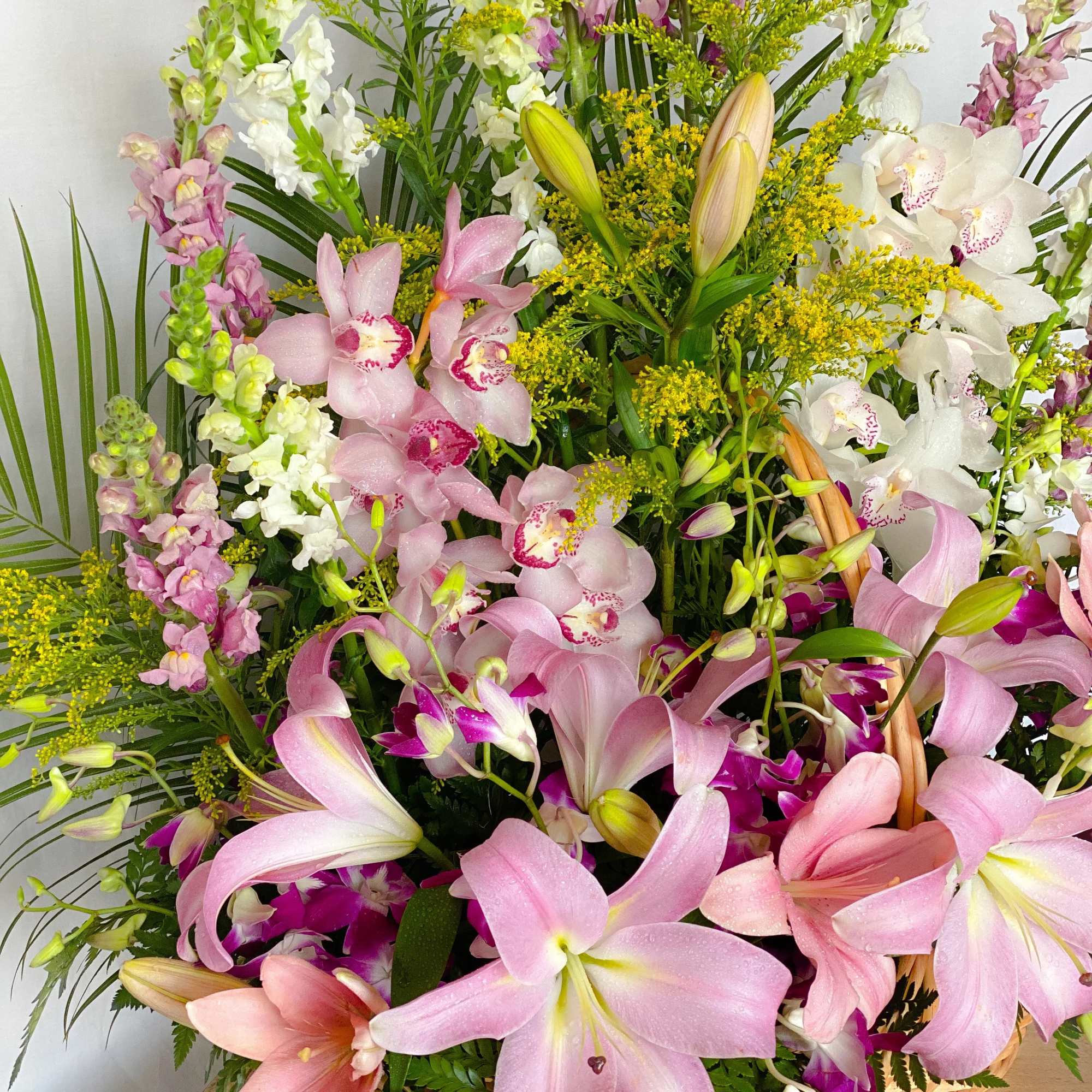 Basket arrangement of pink lilies, orchids, and white snapdragons
