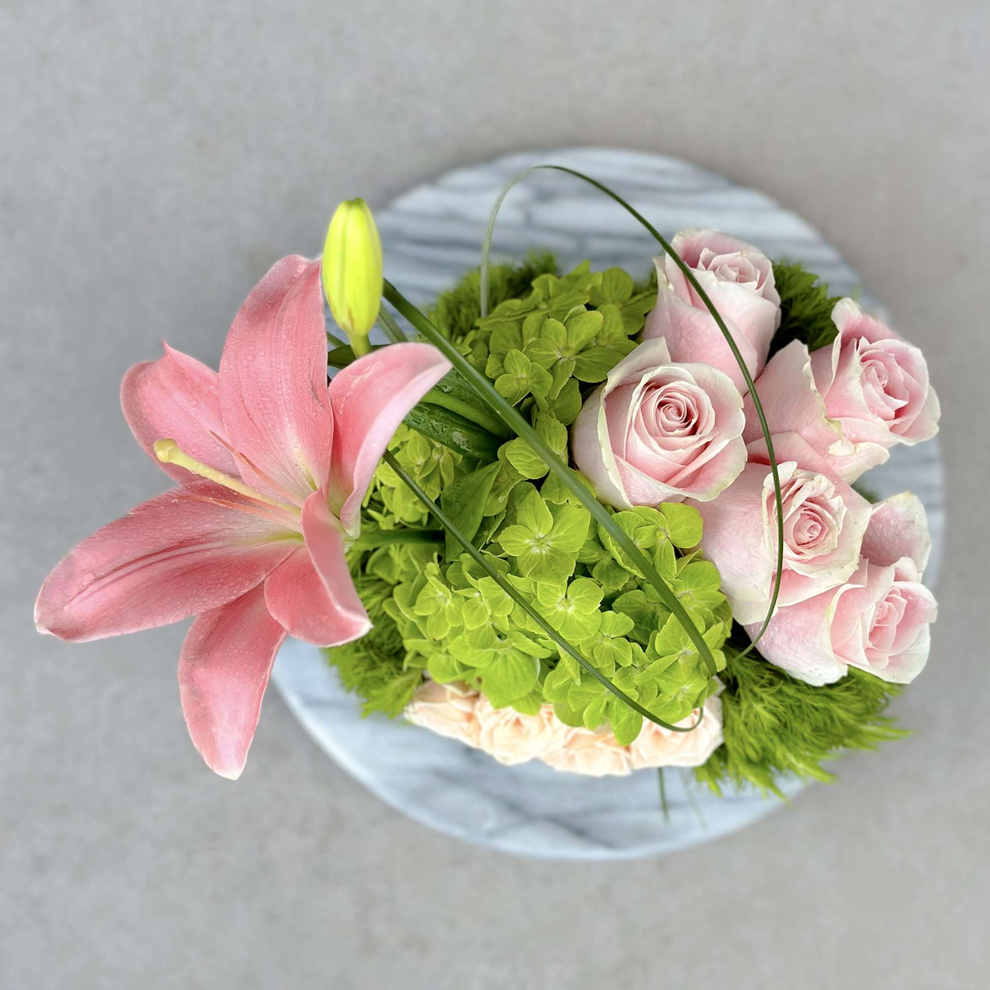Pink lily and roses arranged in a round vase