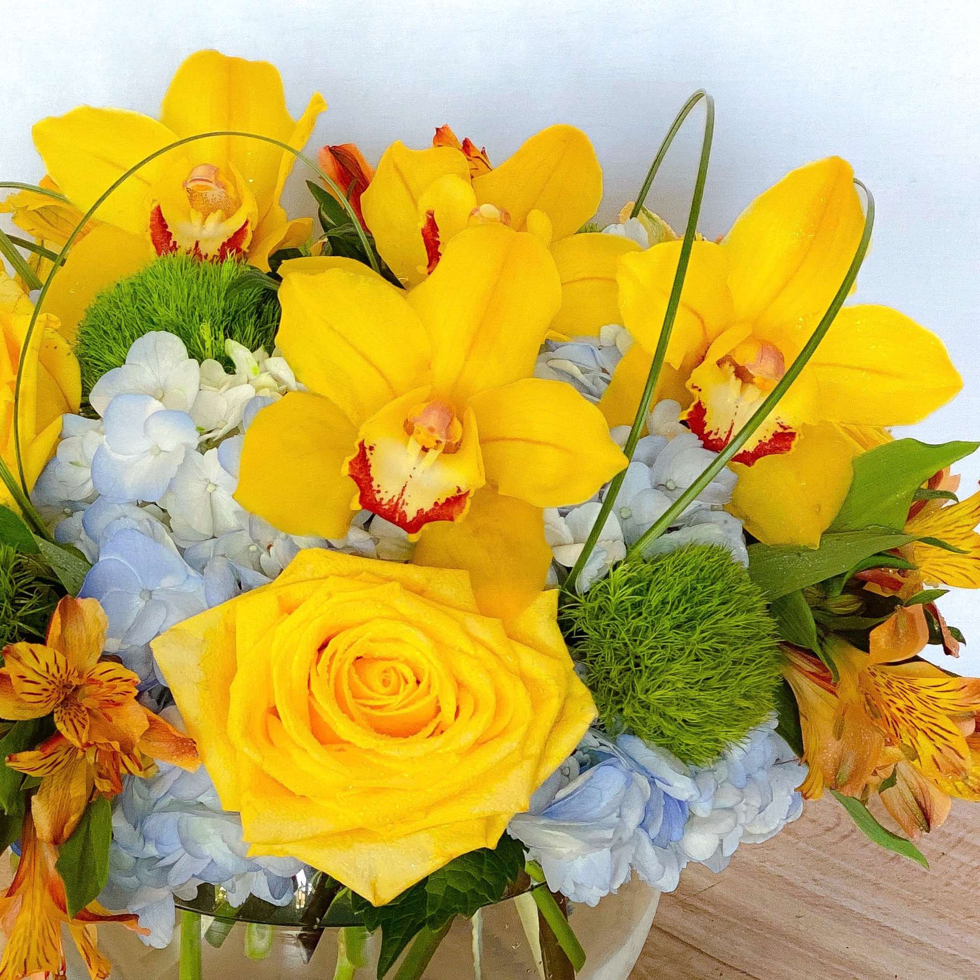 Yellow orchids and roses arranged with pale blue hydrangeas in a glass vase