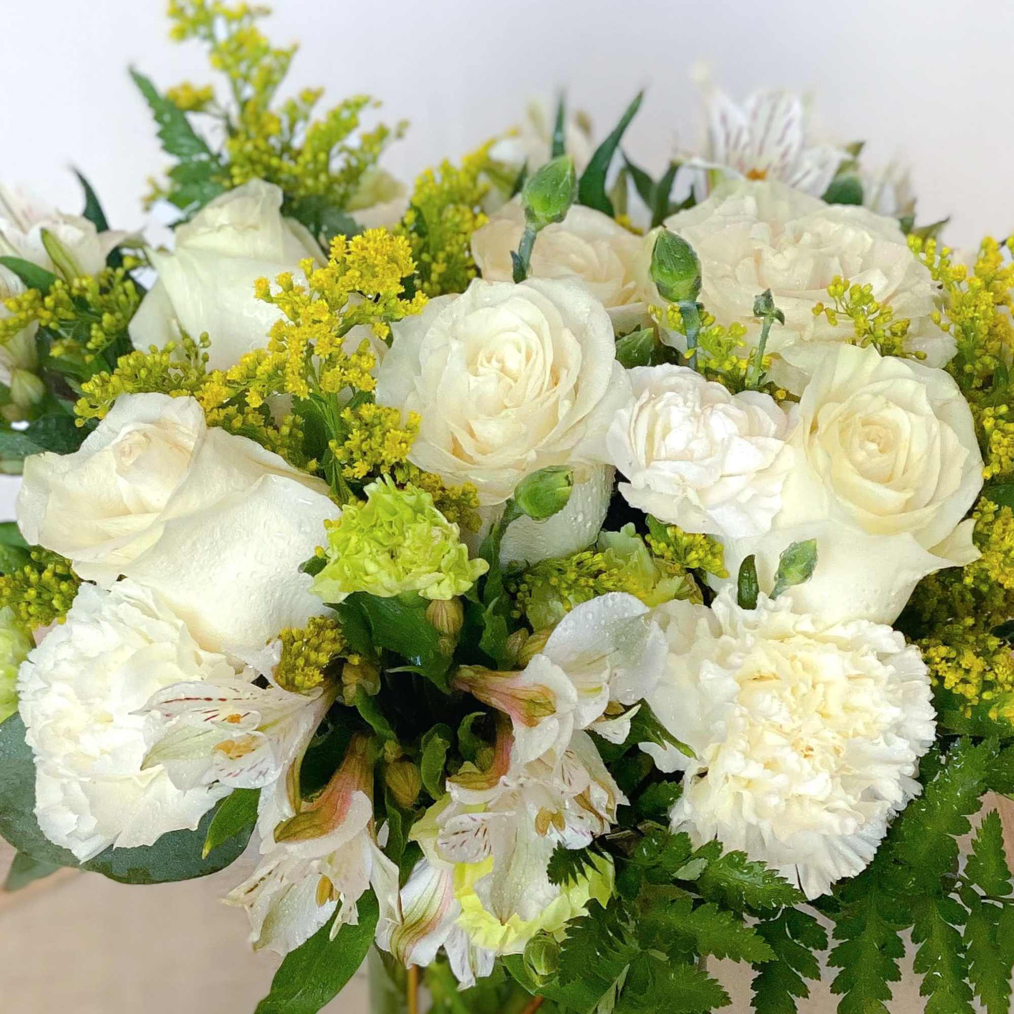 White roses and carnations with yellow filler flowers in a bouquet