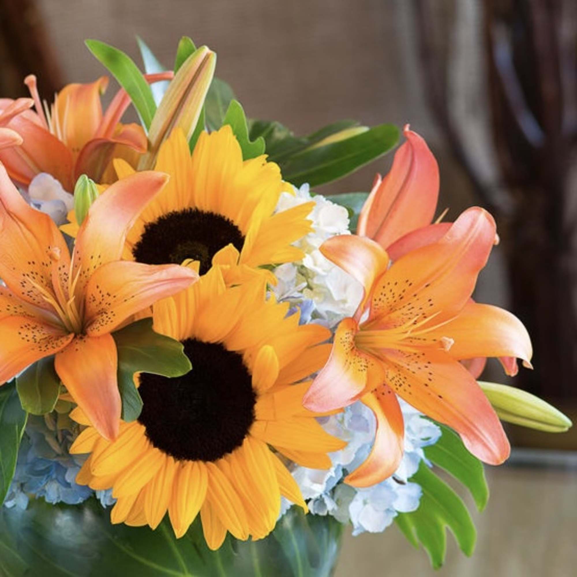 Bouquet of sunflowers, orange lilies, and blue hydrangeas in a vase