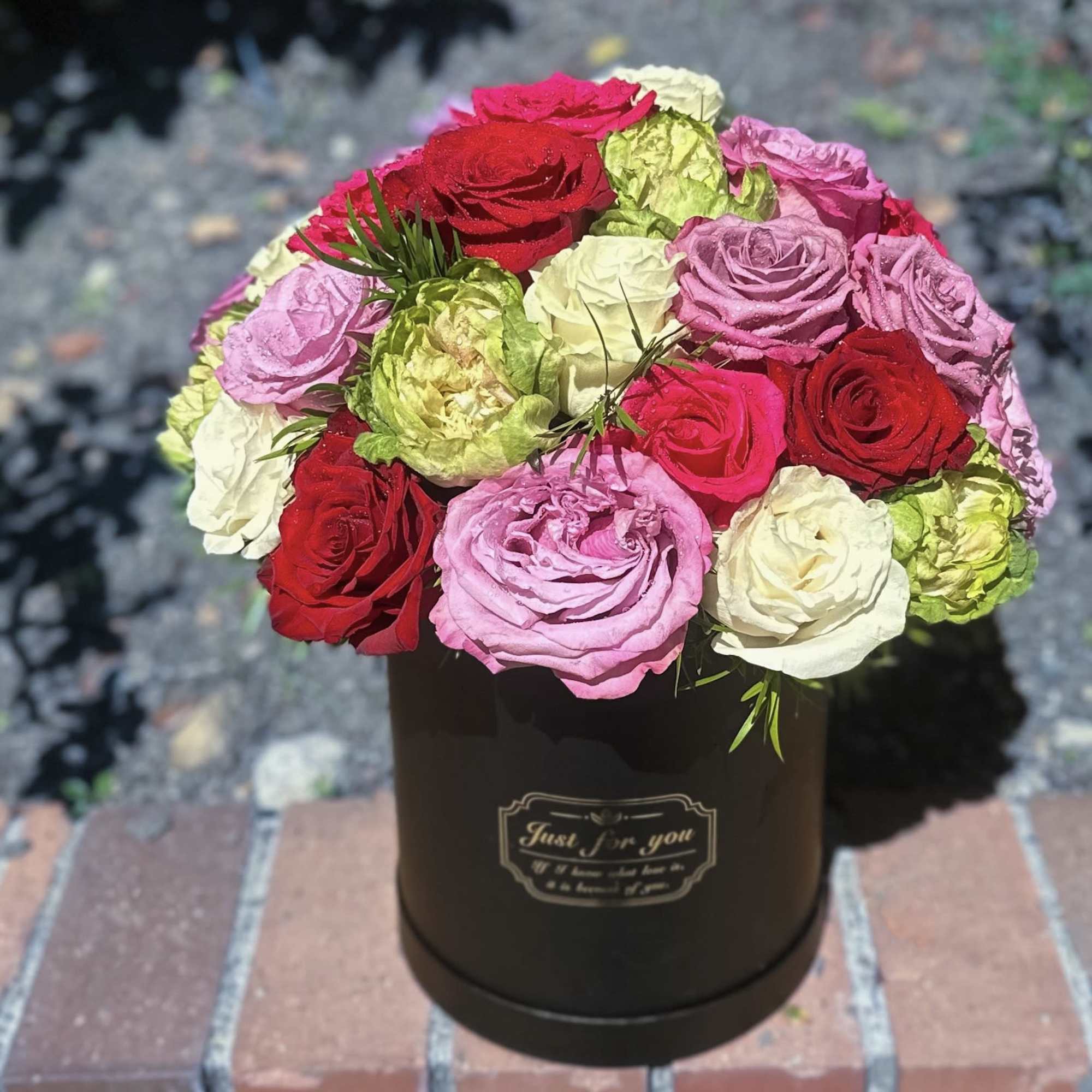 Mixed roses in pink, red, white, and green arranged in a black hatbox