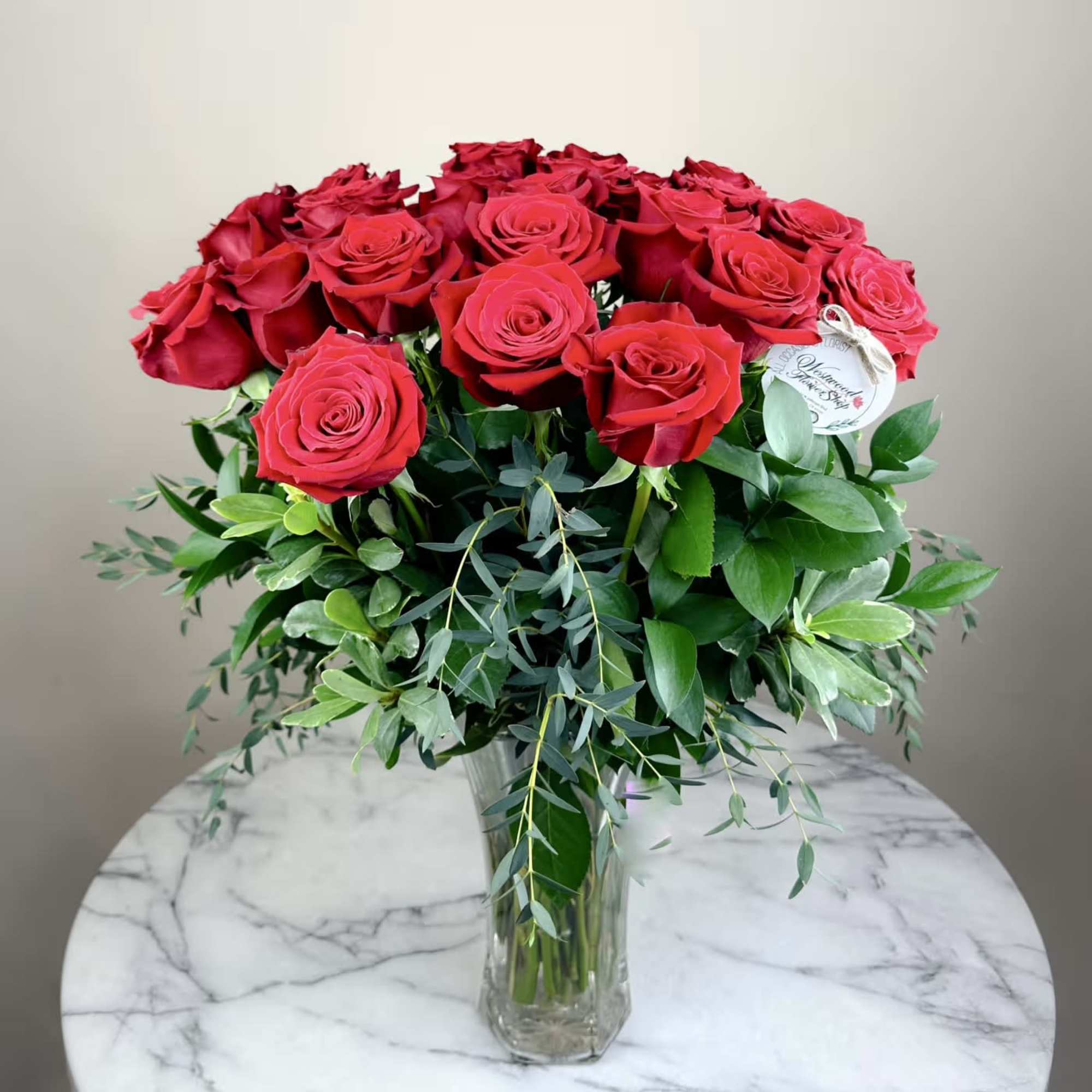 Red roses arranged in a clear glass vase with mixed greenery