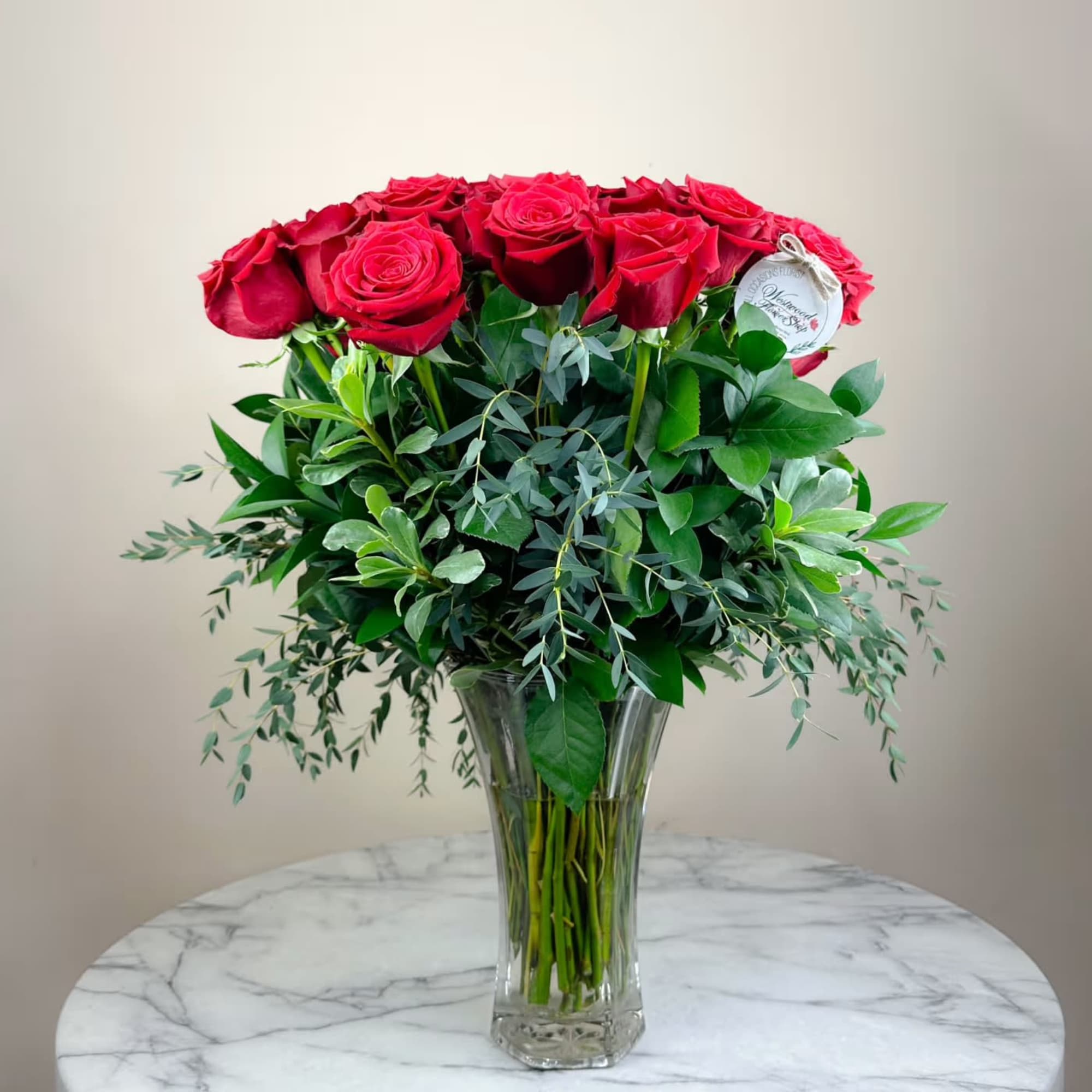 Red roses arranged in a clear glass vase with lush greenery